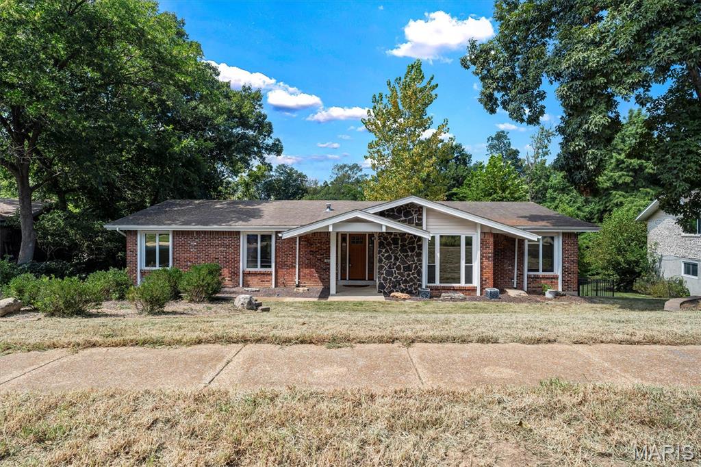 Nestled in Ballwin, 605 Forrester Dr presents a spacious 5-bedroom, 3-bathroom layout. The exterior features a classic red brick facade paired with a dark stone feature wall that frames the covered front porch. Stepping inside, the main floor opens into a sunken front living room detailed with carpeted flooring, stepped access, and a wide multi-pane window fitted with blinds. The kitchen is outfitted with solid wood cabinetry, light quartz countertops, a stone tile backsplash, under-cabinet lighting, and a breakfast bar peninsula. Kitchen appliances include a gas cooktop, overhead microwave, black dishwasher, and black refrigerator. Positioned just off the kitchen, the hearth room features wood flooring a fireplace with a stone surround and wood mantel, and sliding glass doors that open to the back sun room.  The home contains five bedrooms and three full bathrooms. The finished walk-out lower level extends the indoor living area with wood-look flooring, white support pillars, carpeted stairs, and sliding glass doors leading outside. A broad, covered screened-in porch provides protected outdoor space, featuring tile flooring, dual ceiling fans, and roll-down privacy shades. The property is completed by an attached two-car garage.
