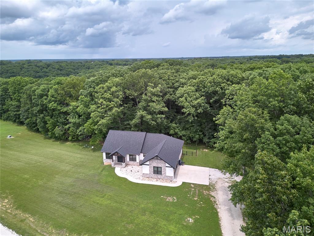 Why wait to build? This custom 2023 Craftsman offers the perfect blend of modern style, privacy, and convenience on 5.6 wooded acres just 1 mile from US-61 and only 20–25 minutes from Wentzville. Step inside to an open-concept floor plan featuring 9' ceilings, abundant natural light, and quality finishes throughout. The kitchen is designed for both everyday living and entertaining with custom cabinetry, granite countertops, a large center island, stainless steel appliances, and an oversized walk-in pantry. The split-bedroom layout provides added privacy, while the spacious primary suite features a large walk-in closet and a spa-inspired bath with a soaking tub, dual vanity, and walk-in shower. The attached garage is equipped with 220-volt electrical service, offering added flexibility for an EV charging station, workshop equipment, or other high-power needs. Relax on the covered back deck overlooking the peaceful wooded acreage, enjoy evenings around the fire pit, or explore the private trail winding through the trees where wildlife is often seen. The full walkout basement with a bathroom rough-in offers endless possibilities for future living space.  Offering the quality of a nearly new custom home, the privacy of 5.6 acres, and a location just minutes from Troy and US-61, this is a rare opportunity you won't want to miss.