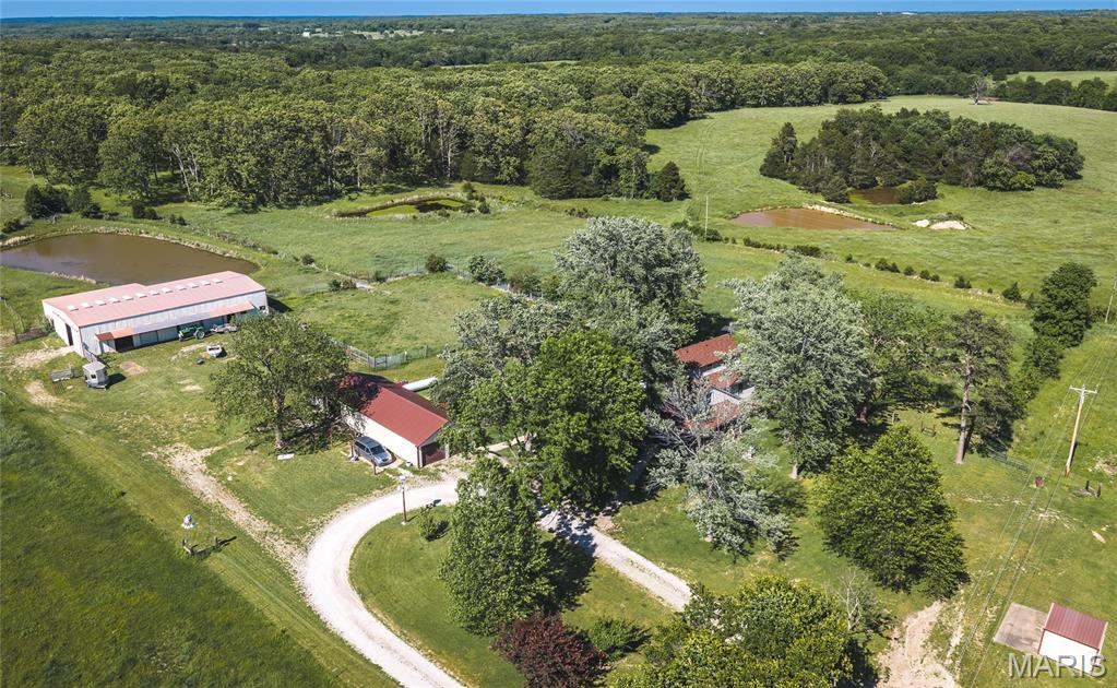 Located on 20.75 +/- acres, this 4 bedroom, 3 bathroom home offers over 3,000 square feet of living space along with the setup and outbuildings that are hard to find this close to town. The property features open pasture ground, two ponds, mature trees, fenced areas, and a peaceful setting with plenty of usable acreage. The home offers a functional layout with multiple living spaces, office space, and an upstairs with two bedrooms and a full bathroom. The main level offers a spacious primary suite with full bathroom and main level laundry. A large, covered porch overlooks the property and provides a great spot to relax and enjoy the country setting.
Several major updates have already been completed including a roof approximately 3 years old, and a newer HVAC system installed last year. Outside, the property is well suited for equipment storage, livestock, hobbies, or workshop space with a large steel outbuilding measuring approximately 98x40 plus a 17x40 lean-to addition. The building sits on 3' footings and offers approximately 12’6” clearance. There is also a fully insulated detached garage measuring approximately 23x61, an additional older garage, chicken house, and storage shed. If you have been searching for acreage with a spacious home, multiple outbuildings, and a setup that offers both functionality and privacy, this property deserves a look.
