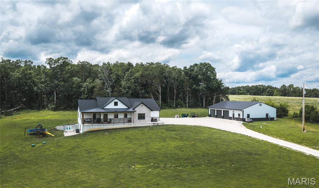 Step into this beautiful newly built home nestled on 5 acres just outside of town, offering the perfect blend of country charm and modern convenience. With 5 bedrooms and 3 bathrooms, there is plenty of room for family, guests, and entertaining. The heart of the home features a spacious open concept kitchen, dining, and living area with hardwood floors, custom soft close cabinetry, stainless steel appliances, a large center island, and a great pull-out drawer pantry. The large master suite provides a private retreat in the divided bedroom floor plan, while the main floor laundry adds everyday convenience. Enjoy seamless indoor-outdoor living with access from the living room to a covered outdoor entertaining space with a double sided fireplace overlooking the above ground pool, perfect for relaxing or hosting family and friends. Take in the beautiful countryside views from both the large covered front porch and covered back patio. The finished lower level offers incredible additional living space, including 2 bedrooms, a large recreational area, storage room, and vault room. You'll also find a dedicated TV/movie room that could easily serve as a sixth bedroom, home gym, or office. Adding even more value is the 2400 sqft shop featuring 3 bays, a framed up half bath, space for a dedicated storage room, office space, and an abundance of shelving, making it ideal for hobbies, a home business, equipment storage, or workshop needs. If you're looking for a spacious home with modern amenities, beautiful views, and room to spread out, this property is one you won't want to miss. Schedule your showing today and experience country living at its finest.
