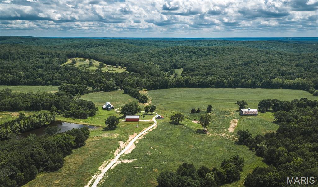 A truly rare offering, this 1,377+/-acre legacy property in the heart of Maries County represents the finest qualities of the Missouri Ozarks—unspoiled beauty, abundant water, productive land, and exceptional sporting opportunities. Held together as a remarkable contiguous tract, this estate offers a combination of scale, natural resources, and character that is increasingly difficult to find.
The historic farmstead serves as the centerpiece of the property, featuring a farmhouse currently utilized as a hunting lodge, several picturesque vintage barns rich with Ozark heritage, and a substantial 40' x 60' shop with concrete floors and electric service. Just behind the home, a beautiful 1.5-acre lake provides both scenic appeal and additional recreational opportunities, creating an inviting setting for family and guests alike.
More than 200 acres of open ground are strategically scattered throughout the farm, including approximately 130 acres of fertile creek-bottom fields. These highly productive soils present an outstanding opportunity for agricultural production, wildlife food plots, or a carefully balanced land management program designed to maximize both income and habitat value.
Water is one of the property's defining assets. A large natural spring feeds a crystal-clear spring-fed pond before joining Long Creek, which courses through the ranch for more than two miles. In addition to the lake and spring-fed pond, several smaller watering holes are distributed throughout the property, ensuring dependable water sources for wildlife and livestock while enhancing the overall diversity of the landscape.
Rolling ridges, secluded hollows, towering timber, and panoramic views define the terrain. A magnificent grove of mature whistling pines overlooks two hidden hollow fields to the North, creating one of the most scenic settings on the farm and a natural gathering place to enjoy the peace and beauty of the Ozarks.
Renowned for its outstanding deer and turkey hunting, the property offers a rare blend of habitat, water, and food sources that support thriving wildlife populations. Whether envisioned as a private sporting retreat, working ranch, recreational getaway, or multi-generational family legacy, this exceptional holding presents an opportunity seldom found in today's market.
With its combination of live water, productive bottomland, historic improvements, and remarkable natural beauty, this is far more than a farm—it is one of the premier large-acreage estates available in Maries County and a property destined to be treasured for generations to come.