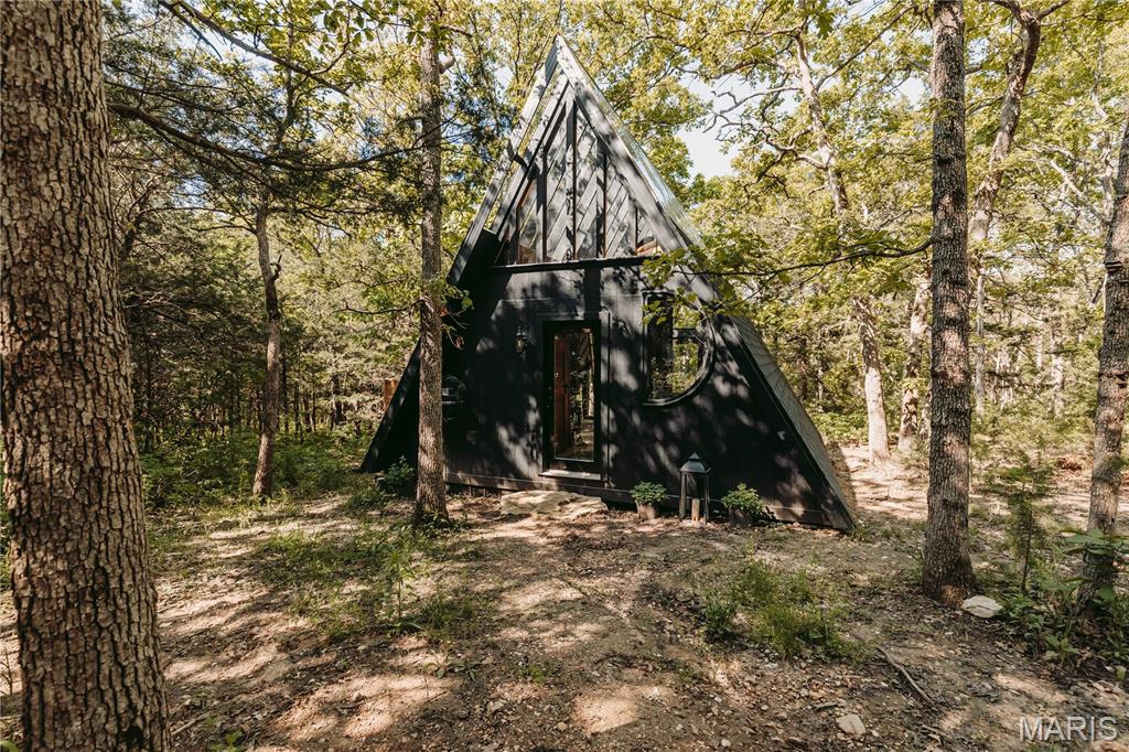 Endless possibilities await on this breathtaking 15-acre wooded retreat. Nestled among mature trees and accessed by a scenic circle drive, this one-of-a-kind property offers privacy, tranquility, and convenient access to the Lake of the Ozarks. The custom A-frame guest home is truly special, featuring a stunning windows in the loft sleeping area, allowing you to fall asleep under the stars. You'll find an inviting foyer, open-concept living space, kitchenette, custom-tiled bathroom, large windows that showcase the surrounding natural beauty, and an outdoor entertaining area perfect for relaxing or hosting guests. A picturesque rock water feature adds to the peaceful atmosphere. With its unique design and setting, the guest home offers exciting potential for personal enjoyment or future rental opportunities. The three-story A-frame main home is ready for new owners to bring their vision to life and complete this dream property. Whether you're seeking a private residence, family retreat, vacation getaway, or investment opportunity, the possibilities are endless. Experience the beauty, serenity, and potential of this remarkable property.