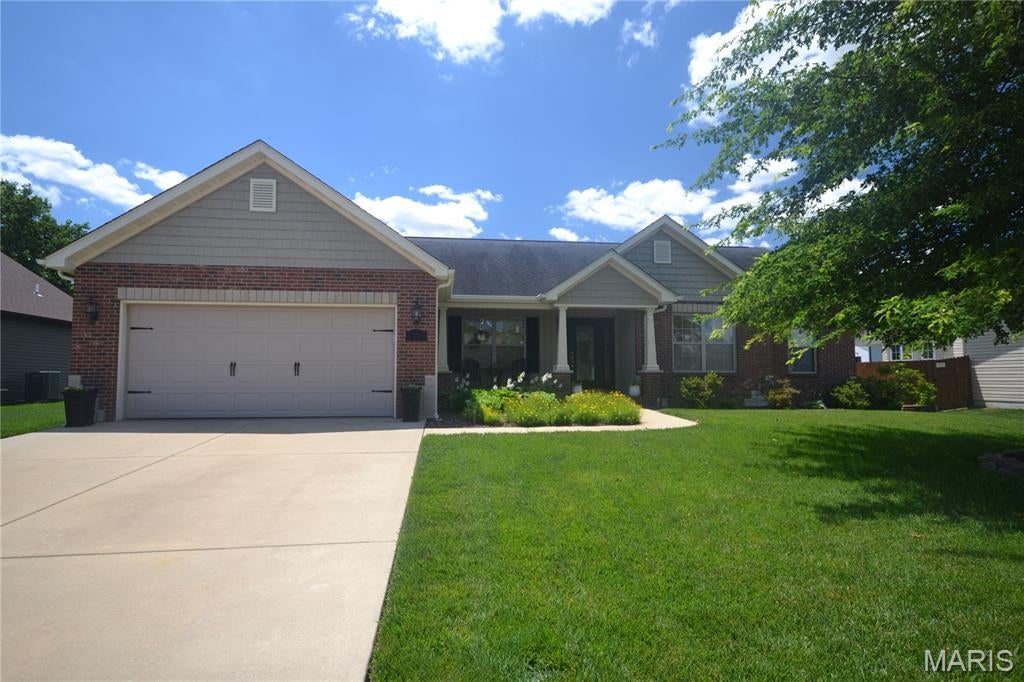 A former model home of exceptional presence, this South Woods residence blends refined architectural detail with warm, inviting elegance—crafted to impress from the very first glance.

Beyond its beautifully manicured landscaping and stately covered porch, the home opens to a grand foyer dressed in newer luxury vinyl plank flooring that flows gracefully throughout the main living areas, creating a seamless, upscale aesthetic.

The Dining Room, open to both the foyer and Great Room, offers an elevated setting for intimate dinners or sophisticated entertaining. Just beyond, the Great Room rises with a cathedral ceiling and showcases a dramatic floor-to-ceiling double-sided fireplace, finished in stacked stone—an architectural centerpiece framed by a wall of windows overlooking the serene backyard.

The Kitchen is both stylish and functional, featuring a center island, full appliance suite, and an expansive Breakfast Room that invites natural light and opens directly to the patio for effortless indoor-outdoor living.

The Primary Suite is a private retreat, offering a walk-in closet, ceiling fan, and a spa-inspired bathroom with a separate shower and soaking tub. Secondary bedrooms are bright, spacious, and thoughtfully positioned near the hall bath.

The lower level provides exceptional potential, with a half bath, egress window, sump pump with backup, and radon system already in place—ideal for future luxury expansion.

Outdoors, the backyard is a sanctuary of its own, offering space for gardening, play, or relaxation. A beautiful gazebo anchors the space, creating a perfect setting for alfresco dining or quiet evenings under the stars. An attached two-car garage completes this distinguished home.