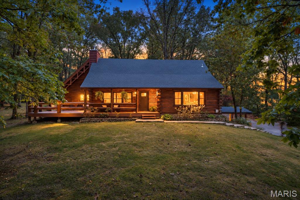 Welcome to the log home that makes everyone who visits want to stay—the kind of place where lifelong memories are made! Nestled on approximately 2.5 acres within a private, gated lake community, this one-of-a-kind retreat offers exceptional indoor and outdoor living. The community is centered around an approximately 200-acre lake, Jefferson County’s largest private recreational lakes. The property includes five lots surrounding the home, four additional lots behind it and a bonus lot across the street providing lake access. A storage shed is ready for your fishing gear, lake toys and outdoor equipment.
From the moment you arrive, the home’s rustic character is unforgettable. A welcoming 22' x 8' covered front porch leads to an impressive 17' x 32' wraparound deck featuring beautiful log railings and plenty of room to relax, entertain and enjoy the peaceful surroundings. Step inside to soaring ceilings, striking log construction and a magnificent stone wood-burning fireplace that creates a warm and inviting gathering space. The bright, open kitchen features a charming bay window, while the main-level primary suite offers a relaxing, spa-like bath. A beautiful wood staircase leads to the upper-level bedroom with its own private full bath, all overlooking the main living area. A convenient main-floor laundry completes the original living space. An approximately 1,000-square-foot addition provides outstanding flexibility for multigenerational living, extended-stay guests or a private suite. Complete with its own entrance, the addition features a spacious family room with a fireplace, kitchenette, guest bedroom with a walk-in closet and a full bath. The staircase was designed and handcrafted by local artist Ryan Meyer of The Wood Den, adding another distinctive touch to this remarkable home. Upstairs, you will find an additional gathering space that could also serve as an office or extra sleeping area when needed. The lower level offers a spacious recreation area with another fireplace, sure to become a family favorite. The garage features a newly added epoxy floor, workshop area and plenty of storage. The community offers pickleball, basketball, fishing and hiking, along with something even more valuable—the opportunity to slow down and enjoy everything you have worked so hard for. You are not simply buying a house; you are choosing a home where friends and family will gather and where children and grandchildren will create stories they will talk about for years. Come experience it for yourself—you may never want to leave!