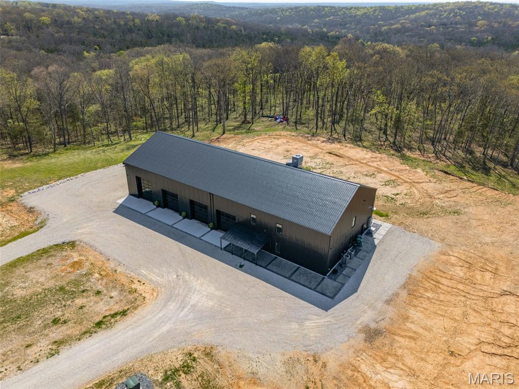 Experience the ultimate blend of modern luxury and private country living with this extraordinary new construction barndominium, set on an impressive 96 acres of rolling woods, open ground, and scenic creek views. This one-of-a-kind property delivers bold architecture, high-end finishes, and exceptional craftsmanship in every detail—creating a true retreat designed for both everyday living and unforgettable entertaining. Inside, the open-concept design showcases soaring ceilings and heated concrete floors throughout. The designer’s chef’s kitchen is a statement space, featuring custom cabinetry, stamped concrete countertops, and a spacious walk-in pantry. The great room is anchored by a striking concrete feature wall with an electric fireplace, seamlessly flowing into the dining area and a large custom bar—perfect for hosting gatherings of any size. The primary suite offers a peaceful escape with a walk-in closet and a spa-like bathroom complete with a soaking tub and oversized walk-in shower. A second bedroom, full bath, and laundry room completes the main level. Upstairs, enjoy a versatile loft living area, third bedroom, additional sleeping room, extra storage, and a unique slide feature that adds both fun and character to the home. The heated and cooled four-bay garage—including a 14-foot door—provides ample space for trucks, recreational vehicles, boats, and equipment. Beyond the home, the land truly sets this property apart. The 96 acres offer a rare combination of mature timber, open fields, and a tranquil creek, creating the perfect setting for outdoor recreation and entertainment. Explore the private acreage ideal for ATV riding, hiking, or horseback use. Enjoy hunting opportunities with abundant wildlife or create your own outdoor oasis with space for firepits, shooting areas, camping sites, or future cabins. Whether you envision weekend retreats, large family gatherings, or a private getaway built for adventure, this property delivers unmatched versatility. The mix of wooded privacy and open terrain also presents incredible potential for investors, developers, or those looking to establish a multi-home family compound, with the possibility to subdivide.