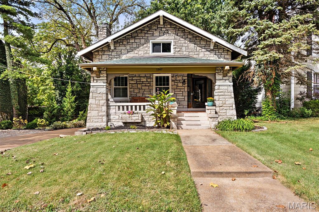 Set on a rare double lot at the edge of Dogtown, this 1920 stone bungalow pairs the craftsmanship of its era with a full suite of modern updates. The deep front porch, framed by massive stone piers and original tapered columns, sets the tone for a home that has kept its character intact: high ceilings, historic millwork, hardwood floors, and a wood-burning fireplace anchoring the living room.

The kitchen was completely renovated and expanded with custom cabinetry, solid-surface counters, a breakfast bar, stainless gas appliances, and a butler's pantry connecting to the dining room. With 2,200 square feet above grade, the layout offers four generous bedrooms and 2.5 baths, including two main-floor bedrooms and a second-floor addition housing a 17x24 primary suite, a second guest room, and an updated full bath with walk-in shower. A partially finished lower level adds another 560 square feet of flexible space.

Out back, a fenced yard opens onto a stunning stone patio with a built-in grill, fire pit, and multiple seating areas beneath mature shade trees, plus wide-open sunset views across the double lot. An oversized attached garage and a driveway turnaround pad handle parking with room to spare.

The list of improvements runs deep: new roof with gutter guards (2022), new first-floor hardwoods (2021), new guest bathroom (2023), built-in window coverings in the front room (2021), glass block basement windows (2024), an enclosed mudroom with new doors and walls (2024), plus updated windows, gutters, plumbing, and A/C.

All of this in a walkable neighborhood just minutes from Forest Park, Maplewood, the Hill, and Highway 40/64. Historic charm, modern comfort, and a lot you won't find twice.