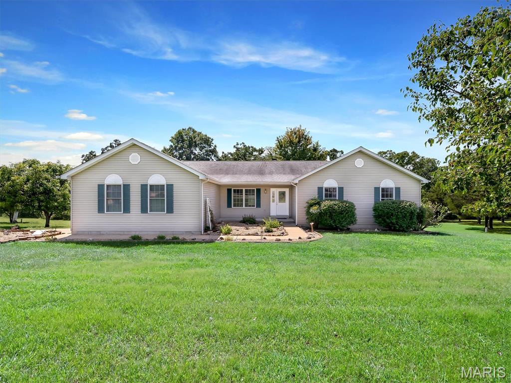 5.15 acres, a private wooded backdrop, and room to breathe—this is the kind of setting that makes you want to stay awhile. Tucked into a quiet subdivision just minutes from Hwy 67, this spacious 3-bedroom, 2-bath home combines peaceful country surroundings with an open, comfortable floor plan made for everyday living and entertaining. Step inside to a dramatic vaulted Great Room where hardwood floors and a floor-to-ceiling stone wood-burning fireplace create an impressive centerpiece. The open layout flows into a generously sized kitchen and dining area with abundant cabinetry, breakfast bar and plenty of room to gather. Just beyond, doors lead to one of the home's best features—a large covered deck overlooking the beautiful acreage and wooded surroundings. It's an inviting spot for morning coffee, outdoor dinners or simply enjoying the privacy and wildlife. The main level offers a spacious primary suite with walk-in closet and private bath, two additional bedrooms, a second full bath and convenient main-floor laundry. An attached 2-car garage, paved driveway and additional parking provide plenty of practicality. Downstairs, the full walkout lower level opens directly to the backyard and offers tremendous potential for additional living space, recreation, bedrooms or a home office. It's already roughed in for a third bath and includes two egress windows. Outside, the gently rolling 5.15-acre property provides the space you've been searching for without sacrificing neighborhood convenience. Come experience the privacy, possibilities and peaceful setting of 114 E Ledge Rock Dr.