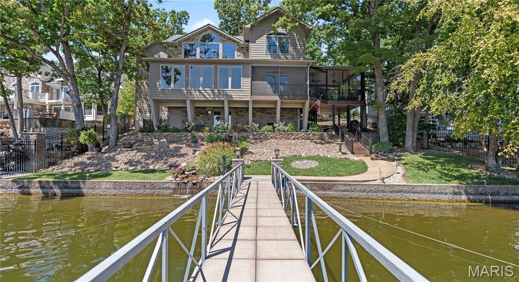 Perched on a premier stretch of shoreline at the 3.5 MM in the Four Seasons, this 4 bedroom, 4.5 bath estate seamlessly blends modern elegance with timeless lakefront living. Recently reimagined with a brand new kitchen addition, the home showcases high end appliances, custom cabinetry, and refined finishes that exude sophistication at every turn. The main floor offers the ease of single level living with two bedrooms connected by a Jack & Jill bath and a luminous living room framing sweeping lake views through expansive windows. With its coveted east facing orientation, mornings are best enjoyed with coffee in hand as the sun rises across the water. Designed for connection to the lake, the layout ensures you can admire the views from multiple vantage points throughout.
The upper level is devoted to a private primary retreat, while the lower level expands the lifestyle experience with a spacious living area, dedicated office, and a home gym. Notable features include geothermal heating and cooling, a serene waterfall, and dual irrigation systems for both the manicured yard and potted gardens along the dock. At the shoreline, luxury living continues with a two well dock featuring dual PWC lifts and a lakeside bar with running water, perfect for entertaining in style. Nestled in the sought after “Power Line Cove,” known for its deep water and reputation as a premier gathering spot, this residence embodies lakefront sophistication at its finest, where every detail has been curated for beauty, comfort, and distinction.