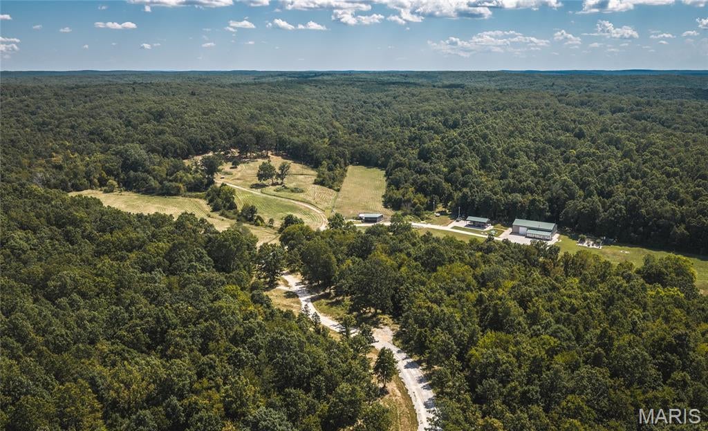 Discover the possibilities at Salem Ranch, an impressive 218-acre property in Dent County, Missouri, conveniently located in Central Missouri, along paved State Route 32 and approximately 30 miles south of I-44. Straddling Lynch Valley and just minutes from Salem, this property offers a rare combination of productive agricultural ground, marketable timber, exceptional hunting, multiple residences, and extensive improvements. Approximately 12% of the property is cropland and 88% timber, providing both agricultural productivity and significant recreational and timber value. The lowland cropland offers fertile ground for producing quality hay, while the timber is readily accessible and offers immediate income potential. The property is bordered on two sides by Mark Twain National Forest, adding approximately 5,000 acres of additional forested ground and creating an exceptional setting for outdoor recreation. With abundant habitat and direct access to surrounding forestland, this is an outstanding area for white-tailed deer and turkey hunting. The acreage is improved for agricultural and livestock use, featuring perimeter fencing, three fenced animal areas with water troughs, and three ponds. A spacious double-gated entrance provides easy access from the paved highway. Cell service is also conveniently accessible with a tower approximately 1,000 yards away. The primary home offers a high-efficiency mini-split HVAC system, electric water heater, electric stove, and 200-amp electrical service. Heavy spray-foam insulation and metal gutters enhance the home's functionality, while an auxiliary wood stove provides an additional heat source. The home is approximately 4,176 square feet of total space, including 2,736 square feet of finished living area and a 1,440-square-foot attached garage/shop. The home features five bedrooms, two bathrooms, a pantry, and an expansive great room measuring approximately 16' x 36' with impressive 18-foot ceilings. A spacious 42' x 12' front porch with 15 large windows and HVAC provides an inviting place to enjoy the surrounding property. The attached 1,440-square-foot garage/shop features 18-foot ceilings, approximately 40 feet of wood shelving, and 30 feet of work benches—ideal for equipment, projects, storage, or a home-based operation.  Outside there is an impressive 24' x 40' pavilion. The pavilion is built on a concrete pad with a metal roof/enclosure and is equipped with stainless-steel amenities including a grill, griddle, sink, refrigerator, and trash drawer. Decorative rock veneer and concrete counters create an ideal space for entertaining, outdoor cooking, family gatherings, or hosting hunting groups. Adding even more versatility is a 2016 Champion Ridgecrest LE II hilltop cabin, offering approximately 1,642 square feet with four bedrooms and two bathrooms. The cabin includes HVAC, 200-amp electric service, septic, and a large 54' x 18' decorative concrete back porch, making it an excellent guest residence, hunting retreat, or additional family accommodations.
Improvements: An open 12' x 60' trailer pad with electric and septic at the well location, and a 12' x 40' metal hay barn. 
Whether you're searching for a working farm, hunting retreat, timber investment, family compound, recreational property, or private rural escape, Salem Ranch offers an exceptional combination of land, improvements, accessibility, and surrounding public forest. Properties of this size and versatility, with direct proximity to Mark Twain National Forest and multiple residences and improvements already in place, are increasingly difficult to find. Salem Ranch is more than acreage—it is an opportunity to own a substantial piece of the Missouri Ozarks with room to farm, hunt, work, entertain, and enjoy the outdoors.