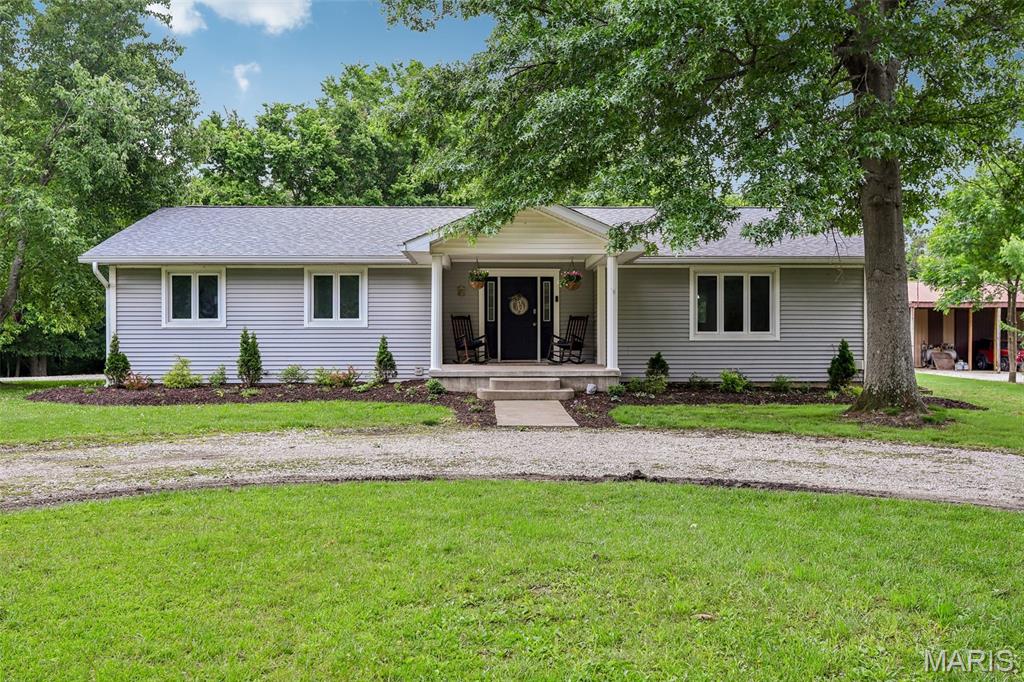 Sitting on just over an acre tucked into the woods near Lake Lou Yaeger, this 3 bedroom, 2 bath ranch has the kind of private setting most buyers are looking for. A covered front porch welcomes you in, and inside an open layout connects the living and dining areas with tons of natural light pouring through oversized windows that look out into the trees. The kitchen is roomy with plenty of oak cabinetry, a built-in wall oven with microwave, cooktop, and a dedicated desk nook, appliances stay. Out back, a spacious stamped concrete patio sets the stage for outdoor living, with a separate pea-gravel fire pit area just beyond. There's a raised garden with arched trellises, a chicken setup, and a walking trail winding through the woods to Lake Lou Yaeger. Add in the 3 car attached garage with workshop space and full unfinished basement, and you've got room for everything.. vehicles, hobbies, storage, future expansion.