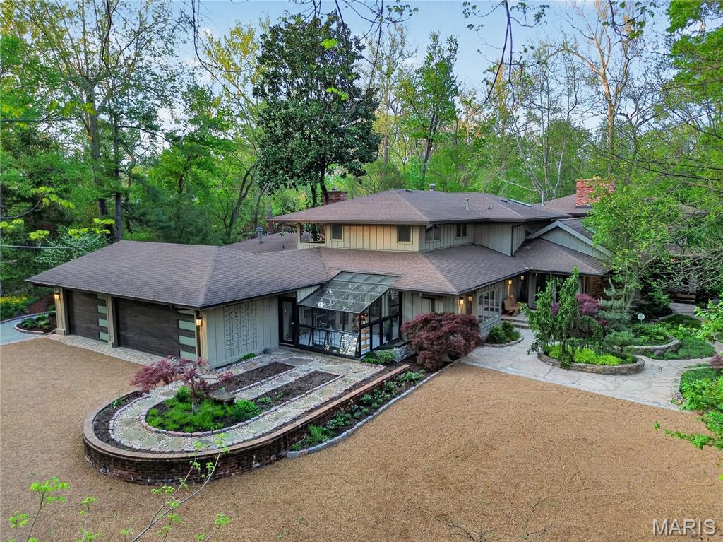 Welcome to this striking contemporary residence set on 2.265 private acres, offering more than 7,400 square feet of refined living space. Designed for both comfort and functionality, the home features five spacious bedrooms, each with its own en suite bath. A light-filled foyer opens to a sophisticated Library lined with floor-to-ceiling built-ins, overlooking the expansive Great Room with fireplace and walk-in wet bar. The open layout creates an effortless flow into the formal Dining Room and a well-appointed Kitchen featuring a center island, premium appliances, a walk-in pantry with freezer, and a bright Breakfast Room with access to the saltwater pool, curated gardens and multiple patios. The kitchen is equipped with two ovens, one with a gas cooktop the other with a warming tray, as well as two dishwashers.  A cozy Hearth Room adjoins the kitchen, providing an inviting additional place to relax. Large windows throughout capture natural light and serene views from nearly every room. The main-level Primary Suite offers a retreat with access to a private courtyard featuring a lovely water feature. Two generous walk-in closets, a spa-inspired bath with heated flooring, and direct access to the pool terrace make the space both practical and cozy. The pool feels like a private oasis - heated saltwater, softly glowing underwater lights, and a built-in sound system that extends throughout the home for a seamless atmosphere. Upstairs, three additional bedrooms each include walk-in closets and private baths; one features its own sitting room, covered balcony, and added privacy. A central hallway leads to an elevated balcony overlooking the grounds. An adjacent wing extends the home’s flexibility with a spacious family room, separate exterior entrance, and private upper-level suite complete with en suite bath, laundry, walk-in closet, and its own balcony—ideal for guests, multigenerational living, or a dedicated work-from-home space. A versatile Bonus Room connects to a brand new 14x10 Hummert greenhouse which offers a professionally designed, high-performance growing environment. Thoughtfully engineered for efficient climate control and airflow, it provides an ideal setting for year-round gardening, whether for dedicated cultivation or personal enjoyment. As you arrive at this special property take a moment to feel the outside world quietly fall away, replaced by a sense of privacy, beauty, and calm. This is not simply a landscape—it is a fully realized garden experience, professionally designed to immerse the homeowner in serenity and refined luxury. The grounds are composed entirely of curated gardens, forming a continuous tapestry of lush plantings and intentional design. Meandering pathways guide you through a sequence of destinations, each offering framed views, layered textures, and moments of quiet discovery. A reimagined multigenerational pool and terrace anchor the setting, while an elegant boardwalk connects sun-filled gardens with shaded woodland retreats.  A mature tree canopy provides cooling refuge, and each area unfolds with purpose, balance, and restraint. Every detail has been thoughtfully orchestrated to enhance daily living—an environment designed not only for beauty, but for how it feels to experience it. A rare and complete pleasure garden, where luxury is defined by experience, privacy, and intention. 
This space is an unbelievable place to call home!