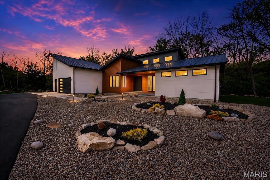 Set on over four private, wooded acres, this brand-new Mid-Century Modern masterpiece redefines contemporary living with architectural precision and effortless sophistication. A long, dramatic drive leads to the striking facade, where clean lines, expansive glass, and impeccably landscaped grounds create a true sense of arrival. A stunning black metal pivot door opens to soaring ceilings and an open-concept plan bathed in natural light from high transom windows. The living room centers around a sleek linear fireplace, while the designer kitchen impresses with custom cabinetry, a sprawling island, and a built-in coffee bar for refined everyday living. The main-floor primary suite is a private sanctuary, featuring its own covered patio, dual walk-in closets, and a spa-worthy bath with a soaking tub encased within a glass-wrapped shower. A stylish laundry and drop zone complete the main level. Upstairs, a lofted office with separate sitting area provides the perfect creative escape, while a breathtaking floating staircase with all-glass railings leads to the finished lower level, offering two bedrooms, a full bath, and expansive recreation space. Outdoors, mature trees and total privacy create an inspiring natural backdrop for future amenities or peaceful retreat. A three-car garage and exceptional craftsmanship throughout complete this modern estate - where design, nature, and serenity exist in perfect balance.