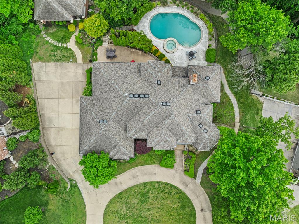 This impressive 6,000+-square-foot brick-and-limestone home is set on 1.29 acres in Sunset Hills and includes a separate 2,000+-square-foot, two-story guest house. The thoughtfully designed layout is ideal for both everyday living and entertaining. Hardwood floors flow through the living and dining areas into the kitchen. The kitchen offers generous cabinetry, extensive workspace, a large walk-in pantry, and a breakfast room open to the family room. The dramatic two-story living room features a two-sided fireplace shared with the family room, while a circular library creates a fun spot for reading or working. The main-level primary suite includes dual vanities, a soaking tub, a separate shower, and walk-in closets. Upstairs, a loft overlooks the foyer and leads to three bedrooms - one with an ensuite bath and two joined by a Jack-and-Jill bath. The walk-out lower level expands the living space with a family room featuring a fireplace, a bar area, a bedroom, and a full bath. The guest house offers exceptional flexibility, with a private apartment above featuring a full kitchen and bath, and a freshly painted wine cellar below with a barrel-vaulted ceiling. Outdoor amenities include a pool and spa, plus a lower, level yard with a swing set.