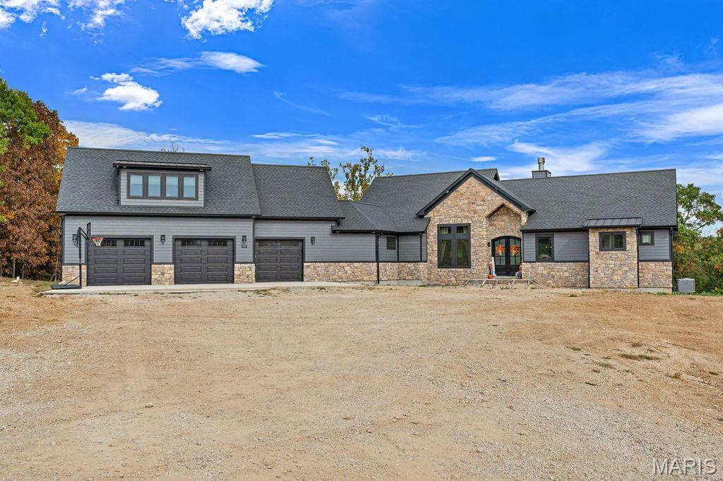 A true Masterpiece in Hidden Ridge! Nestled on 7.85 acres of rolling countryside just east of Washington, Missouri, this jaw-dropping custom-built 1.5-story home offers over 2,700 square feet of thoughtfully designed living space where craftsmanship, comfort, and natural beauty meet in perfect harmony. From the moment you arrive, the home’s commanding presence and stunning stone-and-wood exterior set the tone for what lies within. Inside, a warm yet sophisticated atmosphere unfolds—anchored by a striking floor-to-ceiling stone fireplace and enriched with custom finishes at every turn. The open-concept kitchen is a showpiece, featuring custom-painted cabinetry, an oversized island perfect for gathering, tile backsplash, solid surface tops, and a generous walk-in pantry. The great room soars with tongue-and-groove vaulted ceilings, flooding the space with light and accentuating the home’s spacious flow. The main-floor primary suite offers a serene retreat with its own vaulted ceiling, dual walk-in closets, and a luxurious ensuite bath complete with a double vanity and expansive walk-in shower. A dedicated office area provides an ideal space for working from home or creative pursuits. Upstairs, the bonus area above the garage offers incredible versatility with a family room, two additional bedrooms, a full bath, and even a laundry space—ideal for guests, older children, or extended stays. Every room has been designed to capture the breathtaking views that surround the property, creating a seamless connection between the indoors and nature’s beauty beyond. The oversized 3-car garage provides a true zero-step entry into the home for ease and accessibility. For those who dream of extra space to entertain, create, or store, the impressive 45’x140’ detached garage opens endless possibilities—from car collections to workshops, gatherings, or future expansion. This exceptional property combines the allure of modern luxury with the tranquility of a private, countryside setting. Whether enjoying a quiet evening by the fireplace, hosting gatherings under the vaulted ceilings, or taking in panoramic sunsets from your own backyard, every moment here feels extraordinary. A rare opportunity to own a custom estate of this caliber in the Hidden Ridge community—where craftsmanship meets breathtaking views and peaceful living.