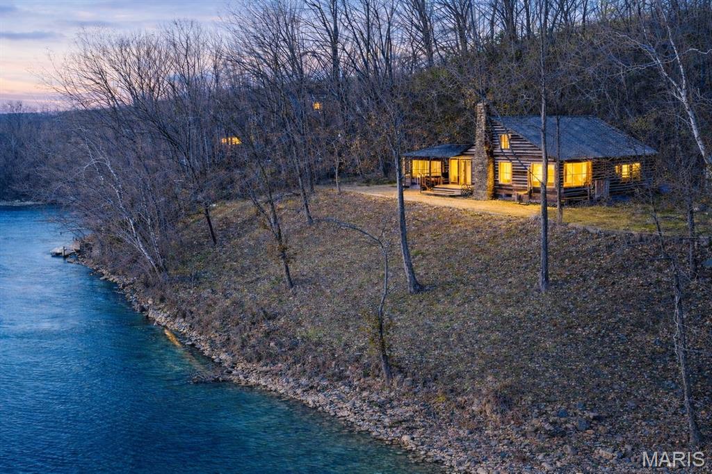 Turn-Key 3BR Log Cabin on the Current River - No Flood Risk - Fully Furnished

Beautifully maintained real log cabin situated directly on the banks of the scenic Current River and just 15 minutes from Doniphan. Enjoy true riverfront living with the rare and valuable benefit of no flood exposure, offering added peace of mind along with unbeatable views and access.

Positioned on approximately .50 +/- acre, this 1,200 +/- square foot cabin features 3 bedrooms and 1 bath, with the third bedroom currently serving as a bright sunroom overlooking the property--ideal for flexible living or guest space. Authentic hardwood floors run throughout, enhancing the warm, rustic character.

The inviting living area centers around a wood-burning fireplace, while upgraded electrical and plumbing systems provide modern reliability. The bathroom has been completely remodeled for updated comfort. The kitchen and entertaining spaces feature granite countertops, a wet bar, and a tankless water heater for convenient on-demand hot water.

Outdoor living is a highlight with two patios and an enclosed porch with electricity--perfect for relaxing, entertaining, or enjoying the river setting year-round. Recent improvements include new insulated windows for efficiency and comfort, along with a water softener system. The property is serviced by private well and septic.

Being sold fully furnished (excluding mounted items), this cabin is truly turn-key for personal enjoyment or continued short-term rental use. With a strong history as a top-rated Airbnb and potential for a private dock (subject to approval), the property offers excellent recreational and income-producing potential.

A rare opportunity to own a move-in-ready riverfront retreat offering location, condition, flexibility, and freedom from common flood concerns -- all directly on the Current River.