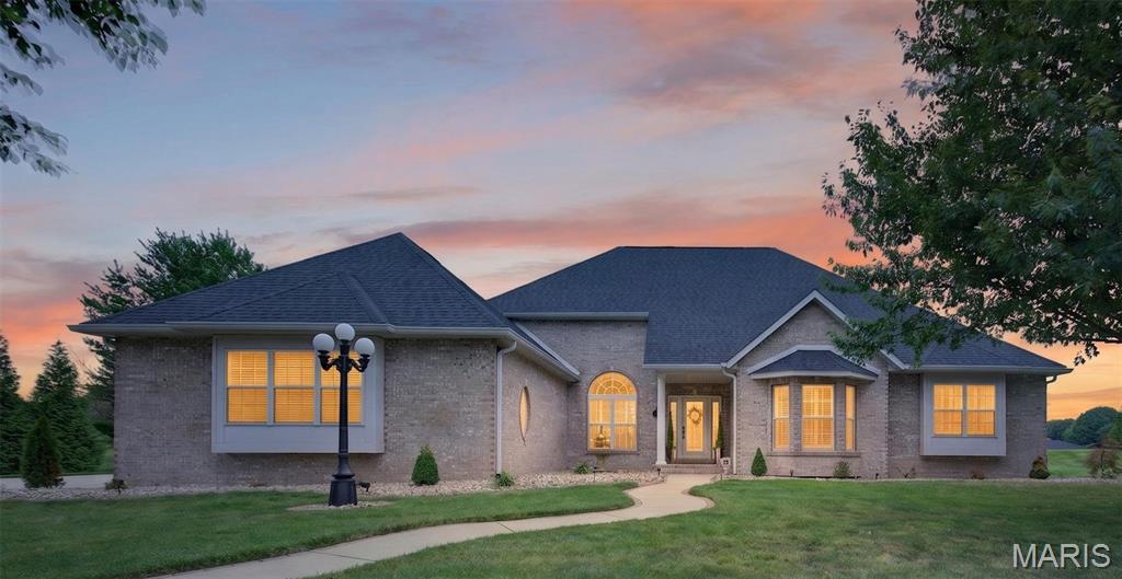 NEW ROOF put on June 2026! Elegant, spacious, and exceptionally maintained, this stately brick ranch presents the perfect opportunity to enjoy luxury living within prestigious Crown Pointe. Perfectly positioned on a quiet cul-de-sac, this 5-bedroom, 4-bath home offers over 5,000 square feet of updated living space on a sprawling .67-acre homesite. Extensive exterior lighting anchored by a classic five-globe lamp post and an opulent water fountain welcomes you home. Step inside to an impressive foyer crowned by a grand chandelier and soaring cathedral ceilings. Newer hand-scraped hardwood flooring gleam throughout the main level while oversized windows with custom plantation shutters fill the home with natural light. Recessed lighting and quality craftsmanship create an atmosphere that is both elegant and inviting. The floor-to-ceiling brick fireplace anchors the great room and serves as the centerpiece of the open-concept design. The chef’s kitchen was built for entertaining, featuring stainless steel appliances, induction stove, high-end countertops by locally renowned K&D Countertops, custom all-wood cabinetry, and island with breakfast bar seating. Adjacent to the kitchen, the versatile hearth/sunroom offers a second floor-to-ceiling brick fireplace and serves perfectly as a dining area, sitting room, or gathering space. The primary suite provides a private retreat with a bay window sitting area ideal for reading or relaxing. The bath features dual vanities, a walk-in shower and separate soaking tub. Additional main-level bedrooms offer generous dimensions, designer ceiling fans, and multiple bay windows. The thoughtfully designed lower level delivers outstanding versatility. A family room is perfect for movie nights and game-day entertaining, complete with a custom bar featuring Corian countertops also by K&D and stylish cabinetry. The recreation area easily accommodates plenty of personal or family fun. A large room with an egress currently serves as a home gym/yoga studio but could easily function as a guest suite, hobby room, or workshop. An additional flex room currently used as a music studio offers possibilities as an office, homeschool area, podcast room, or additional sleeping area. With a full bath already in place, the lower level presents excellent potential for multi-generational living. Recent improvements provide peace of mind, including a newly installed architectural roof and rear siding, an industrial grade sump pump with battery back-up, plus the major systems have been consistently maintained annually. You will equally be impressed by the oversized side entry 3-car garage with electric car hook-up. Backing to a picturesque five-acre family-owned field, the backyard offers some privacy and serves as a blank canvas for your dream outdoor retreat. Imagine a custom inground pool, outdoor kitchen, dining patio, gazebo, or firepit designed for unforgettable gatherings. Conveniently located near parks, trails, golf courses, aquatic centers, hospitals, downtown O’Fallon shopping, restaurants, the Sports Park Complex, and Scott Air Force Base, this remarkable home delivers both luxury and location. Opportunities to enter prestigious Crown Pointe at this price point are rare. Combining elegant finishes, extraordinary living space, exceptional versatility, and one of O’Fallon’s most desirable addresses, this is more than a home—it is a lifestyle ready to be yours.