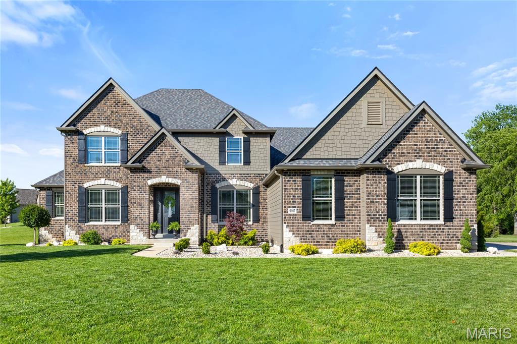 Step into timeless elegance in this exceptional WindCastle residence, where classic Lombardo craftsmanship meets refined modern living. This distinguished brick-and-stone 1.5-story home offers over 4,586 square feet of thoughtfully designed living space, blending architectural sophistication with everyday comfort in one of the area’s most prestigious communities. From the moment you arrive, the home makes a striking first impression with its dramatic covered front porch, professionally landscaped grounds, and extraordinary 8-foot entry door featuring an elegant wrought-iron glass insert. Inside, a grand foyer welcomes you with soaring ceilings, graceful arched passageways, rich acacia hardwood flooring, and finely crafted custom millwork that continues throughout the main level. Just off the entry, a private study creates the ideal setting for a home office, library, or quiet retreat. At the heart of the home, the spectacular two-story great room is designed to impress. A breathtaking wall of windows floods the space with natural light while framing serene outdoor views, and a floor-to-ceiling stone fireplace flanked by custom arched display niches creates a warm yet dramatic focal point. The open-concept layout flows seamlessly into the designer kitchen and breakfast area, creating an ideal environment for both entertaining and everyday living. The gourmet kitchen showcases an exceptional blend of beauty and function, featuring granite countertops, 42-inch espresso cabinetry, premium stainless steel appliances, a stunning stone cooking alcove, oversized 7-foot center island with seating for six, and an adjoining butler’s pantry perfect for hosting gatherings with ease. The adjoining breakfast room is filled with natural light and opens through sliding glass doors to the expansive patio. The luxurious main-floor primary suite offers a peaceful private retreat with an elegant tray ceiling, oversized walk-in closet, and spa-inspired bath complete with dual vanities, soaking tub, and separate shower. Upstairs, the open staircase leads to newly installed carpeting throughout and three generously sized secondary bedrooms, including one private ensuite and two connected by a Jack-and-Jill bath. A spacious bonus loft area provides endless versatility for a media room, playroom, or additional lounge space. The finished lower level features an expansive recreation room, stylish gathering bar, and private guest suite. Every level of the home has been carefully designed to maximize both functionality and comfort while maintaining an elevated sense of style. Perfectly positioned on an impressive .7-acre lot, the outdoor setting is equally inviting with professional landscaping, a spacious patio for outdoor entertaining, and an oversized 3-car garage. This extraordinary residence delivers an exceptional opportunity to experience sophisticated living in highly sought-after WindCastle.