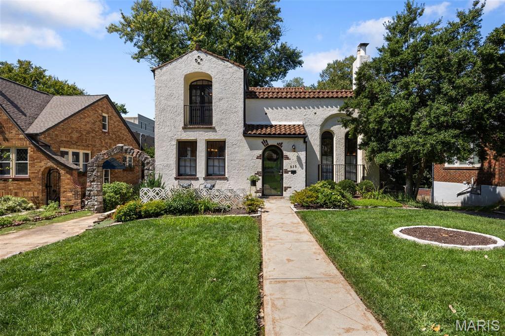 Gracefully blending Mediterranean character with timeless elegance, this exceptional home welcomes you with a distinctive stucco exterior, classic red tile roof, and inviting front porch—perfect for lingering a while and greeting neighbors as they stroll by.
Step inside and prepare to be captivated by the dramatic soaring barrel-vaulted ceiling, handsome gas fireplace, stunning arched windows and stain glass that fill the space with natural light. A unique Juliet balcony overlooks this warm and inviting gathering space, creating an unforgettable setting for entertaining, relaxing, and celebrating special holiday moments.
The spacious dining room is designed for making memories, whether sharing a leisurely meal with friends or gathering around the table for game night. Adjacent, the thoughtfully planned kitchen offers custom cabinetry, stone countertops, and a convenient planning desk that serves as the household command center. A doorway leads to the wonderful shaded deck, extending the living space outdoors—ideal for morning coffee, getting lost in a good book, or dining alfresco. Beyond, beautifully manicured gardens create a lush and tranquil backdrop.
The flexible floor plan offers a wonderful main-level suite featuring charming built-ins, vaulted ceiling, an expansive window overlooking the gardens, and a private atrium door leading directly to the deck. This versatile space could also serve beautifully as a den, family room, or home office, depending on your lifestyle. The updated main bathroom has the comfort of heated floors and shower with convenient bench. 
Ascend to the second floor, where two spacious bedrooms offer generous closet space, hardwood floors, and an abundance of character. French doors open to a delightful Juliet balcony overlooking the mature, treescape-lined neighborhood.
The converted garage adds valuable flexibility, with convenient rear entry and excellent storage space, a possible potting shed for gardening enthusiasts and those who appreciate a place for projects and outdoor essentials.
And then there is the location—truly key to this gem. Ideally positioned near all that University City has to offer and just steps from the Clayton hub of shops, restaurants, parks, and vibrant community life. Enjoy an easy commute to renowned universities and hospitals, with entertainment, culture, and countless amenities close at hand.
Timeless architecture, gracious gathering spaces, beautiful gardens, and an enviable location come together to create a home that is as warm and welcoming as it is distinctive. Start your new story here.