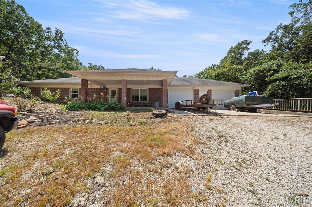 Country Living Just Minutes from Rolla! This inviting ranch-style brick earth berm home offers comfortable one-level living with thoughtful features throughout. Step inside from the covered front porch to an open-concept living, dining, and kitchen area highlighted by a beautiful vaulted wood ceiling. The well-appointed kitchen features a double wall oven, electric cooktop, breakfast bar seating, and eye-catching tin tile backsplash. Several features throughout the home are designed with accessibility in mind, including the spacious primary bedroom with an open closet system and convenient walk/roll-in shower. Generously sized additional bedrooms, a full guest bath, and a laundry/mud room with sink complete the functional floor plan. This home also offers an attached 2-car garage. An outdoor wood boiler provides backup heat and hot water, offering an additional option for managing utility costs. Outside, the detached 2-car garage/workshop provides plenty of room for vehicles, hobbies, projects, or storage and includes a lean-to on each side for additional covered storage. A wonderful combination of country charm, functionality, and convenience—this property is a must see!