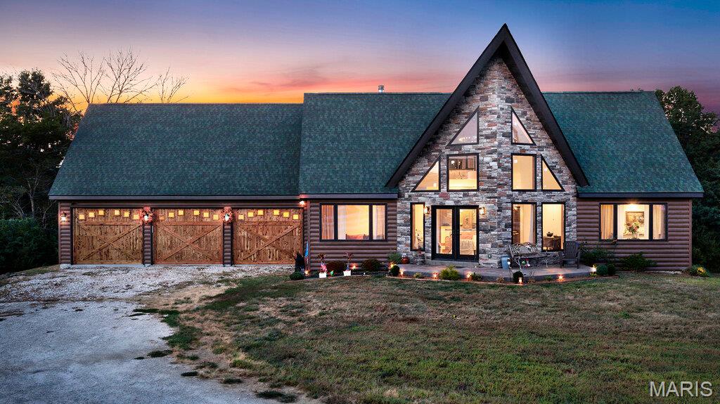 Built in 2023, this striking custom home blends modern lodge, A-frame architecture with rustic craftsmanship, creating a one-of-a-kind property filled with warmth, character and dramatic design. The exterior combines ultra-insulated, log-style siding with an impressive stone-accented A-frame façade, while soaring rooflines and an extraordinary arrangement of geometric windows hint at what awaits inside.

Step into the spectacular great room, where a soaring vaulted, wood-plank ceiling, dramatic walls of windows and a floor-to-ceiling stone fireplace immediately command attention. Natural light pours into the open living space, highlighting the home's exceptional custom wood flooring, featuring rich variations in color and grain that give each room its own distinctive character. A spiral staircase leads to the upper level loft and provides another dramatic architectural element.

The open kitchen continues the home's custom feel with dark wood cabinetry, stainless steel appliances, exposed wood beams and an expansive island topped by an eye-catching blue-and-white epoxy-style countertop. The open layout connects the kitchen effortlessly to the great room, creating an impressive space for entertaining.

Surrounded by oversized windows, the sunroom offers panoramic views of the property and a peaceful place to enjoy the changing seasons. Step outside to the elevated deck for even more outdoor living space.

The primary suite continues the home's distinctive design with an impressive walk-in closet featuring extensive built-in shelving and storage. The adjoining primary bath feels like a private retreat with a large tiled walk-in shower with glass enclosure, corner soaking tub surrounded by windows, wood-plank vaulted ceiling and custom vanity.

Adding even more character is the oversized, 3-car garage three separate rustic wood garage doors, featuring a distinctive carriage/barn-door design, PLUS a 15x8' workshop!

From the dramatic A-frame architecture and soaring wood ceilings to the stonework, exposed beams, custom flooring and abundance of windows, 5 Taylor Ln is anything but ordinary. At 1,980 square feet, this nearly new home delivers the character and craftsmanship of a custom lodge with the advantages of 2023 construction.
The lower level is partially-finished and partitioned with a full bath and walkout.
NOTE: The tax record reports this home as "3 Bedrooms" but it is actually 2 beds on the main level with a "sleeping room" in the lower level.