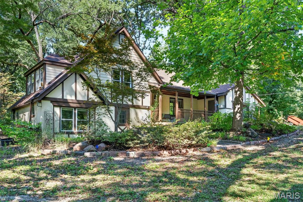 Your own tucked away retreat on 1.74 acres! Set above the street and nestled among mature trees, this three bedroom home offers character, breathing room and an unusually generous amount of land for the area. The beautiful, expansive level backyard is the highlight, with space for gatherings, gardening, outdoor fun or simply enjoying the peaceful setting. A backyard patio and covered front porch offer inviting spots to relax. Tudor inspired details continue the charm, with wood floors, decorative ceiling beams and warm wood trim adding personality inside. A bright sitting area off the kitchen brings in natural light and views of the surrounding trees. An attached garage and separate storage outbuilding add everyday convenience. Livable today with room to make it your own over time, the home needs updates and TLC, with the price reflecting its current condition. If you’ve been searching for more land, a secluded feel and the chance to create something special, this property deserves a closer look. Floor plans located at end of photos. Schedule your showing today!