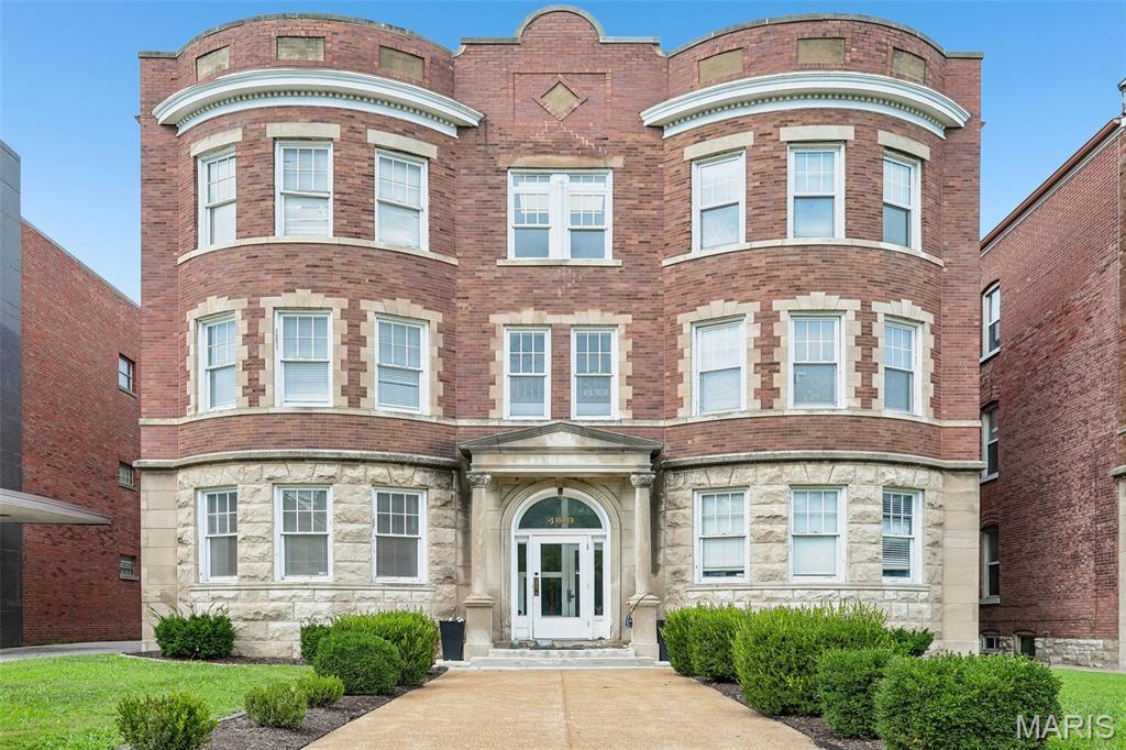 Historic 2-bedroom, 2-bath condo in the heart of the Central West End, Unit H occupies the second floor of a three-story, 1902 brick building at 4319 Lindell Boulevard with a limestone-clad first level and an arched, columned entry portico. The 1,006-square-foot residence pairs the neighborhood's architectural character with in-unit laundry and gated off-street parking. 
Inside, the living room features a wood-burning fireplace with tiled surround, a curved bay window wall with three windows, custom built-in shelving, and crown molding throughout. Hardwood flooring runs through the main living spaces and bedrooms. The kitchen offers butcher block countertops, subway tile backsplash with a decorative tile inset, open stainless steel shelving, a stainless range hood, GE electric range, and a farmhouse-style sink, finished with ceramic tile flooring. The primary bedroom includes a private bath, and a second bedroom with mirrored sliding closet doors shares access to the home's second full bath — two full baths total, each with updated fixtures. In-unit laundry (washer and dryer included) is tucked into its own closet, and central air conditioning with forced-air heat keeps the historic unit comfortable year-round.
Zoned to Adams Elementary, L'Ouverture Middle, and Roosevelt High School in the St. Louis City School District, the home sits amid the Central West End's dining, retail, and medical corridor. It's approximately 0.2 mi to the Cathedral Basilica of St. Louis, 0.6 mi to Whole Foods Market, 0.7 mi to the Central West End MetroLink Station, and roughly 1 mile to Barnes-Jewish Hospital and the Washington University Medical Campus — home to Washington University School of Medicine, St. Louis Children's Hospital, and the Siteman Cancer Center, and one of the region's largest employment centers. Forest Park's 1,300 acres of museums, trails, and green space sit under 2 miles away, with the Euclid Avenue restaurant corridor and Schnucks Lindell grocery also close by.