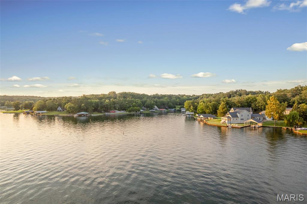 The lake house everyone has been waiting for! Perfectly situated on one of the most desirable waterfront lots at Lake Perry, this exceptional property was designed for making memories. Whether you're looking for a full-time residence, weekend getaway, or the ultimate place to host holidays, reunions, and lake weekends, you'll have the room for everyone. The main home offers an open floor plan, soaring vaulted ceilings, abundant natural light, an impressive floor-to-ceiling stone wood-burning fireplaces that create a warm, inviting atmosphere. The spacious kitchen, dining area and family room flow seamlessly together, making it easy to entertain while staying connected with family and guests. The main level also features an office, full bath, and oversized laundry. Upstairs, the primary suite and three additional bedrooms provide comfortable and privacy for everyone. Step outside to enjoy multiple outdoor living spaces, including a covered patio and screened in porch overlooking the lake- perfect for morning coffee, evening dinners, or simply relaxing while taking in the view. Connected by a covered portico is an impressive guest quarters, giving everyone their own space while still being together. Featuring a soaring wood-vaulted ceiling, floor-to-ceiling stone fireplace, spacious living and dining area, full bath, fifth bedroom, and a large multipurpose room surrounded by windows, this space is ideal for overnight guests, extended family, or additional recreation space. Outside, the amenities continue with with ample parking, a two-car garage, multiple patios, easy access to the water, and a newer covered double-slip dock ready for boating, fishing, kayaking, paddleboarding, or simply enjoying life on the lake. Lake Perry offers something for every generation, including boating, fishing, kayaking, swimming, sandy beaches, volleyball, playgrounds, dining, and countless opportunities to relax and enjoy the outdoors. Conveniently located just 90 minutes from St. Louis and less than an hour from Cape Girardeau, this is more than a lake house- it's a place where generations will gather, traditions will begin, and memories will be made for years to come. Rarely does a property like this become available at Lake Perry. With one of the lake's most desirable waterfront settings, expansive indoor and outdoors gathering spaces, and over 4,000 square feet between the main home and private guest retreat, this is the kind of place where generations of loved ones and friends come together to create lasting memories.