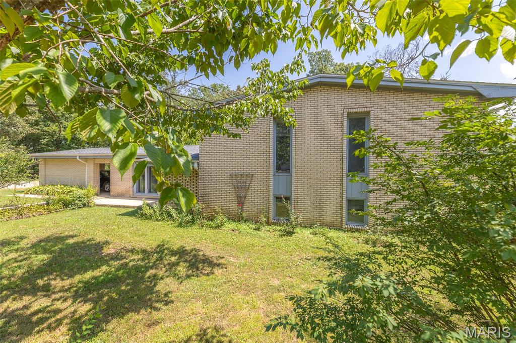 Full of character and timeless mid-century style, this one-of-a-kind tri-level home offers incredible craftsmanship, generous living spaces, and a setting made to be enjoyed. The classic brick exterior and attached carport welcome you inside, where exposed brick and exceptional custom millwork create warmth and character throughout. Step through the front door into the impressive main living area, featuring soaring vaulted ceilings, one of three fireplaces, and large windows that fill the space with natural light. Sliding doors open to the backyard oasis, seamlessly extending the living space outdoors.
Upstairs, you’ll find three bedrooms showcasing beautiful custom millwork, including an oversized primary suite with its own private balcony, the perfect spot to enjoy a quiet morning. Also on this level is a cozy den featuring another fireplace and built-in wood bookshelves that can function as a 5th bedroom if needed. The lower level offers even more room to spread out, with an additional living area centered around the home’s third fireplace, a dining area, kitchen, laundry room, and another bedroom.
Outside, the property continues to impress with a sprawling yard, an additional lot, and two outbuildings offering excellent storage or exciting potential for future guest or living quarters. Best of all, river access provides the perfect place to cool off and make the most of hot summer days. With its distinctive architecture, remarkable craftsmanship, multiple living spaces, and unique outdoor setting, this home is truly a property you have to experience in person!