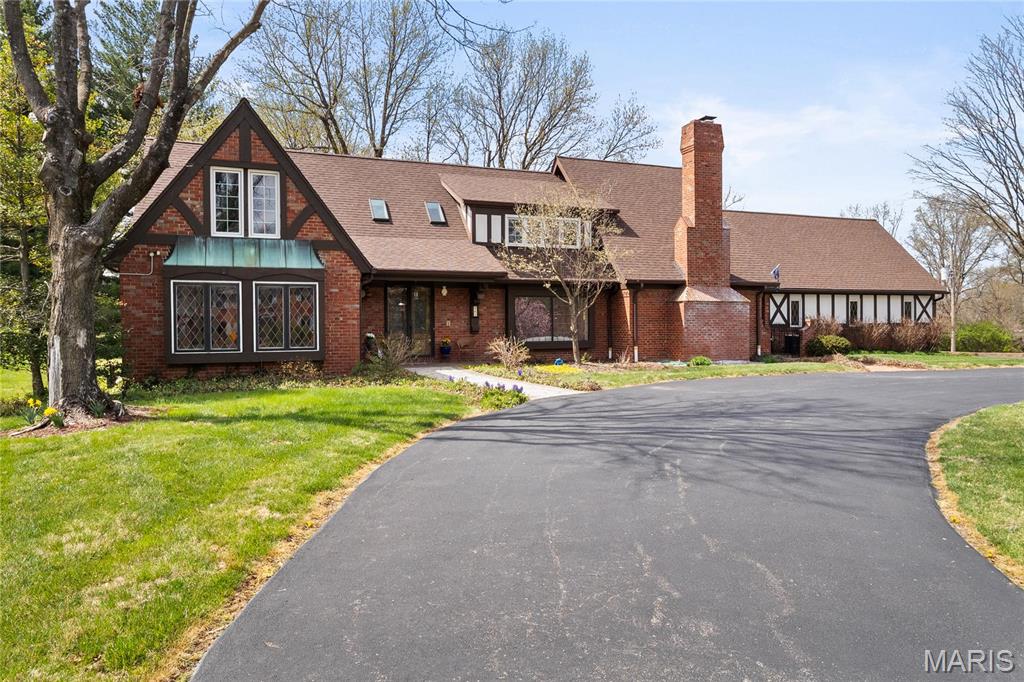 Filled w/classic details, this Tudor-style home will delight! Elegant front doors, reclaimed from an historic downtown building, invite you to enter this substantial home. Sunlight streams through the living room’s large leaded glass window. An even more spectacular stained glass window graces the primary bath. The great room w/ traditional boxed wood ceiling, detailed millwork, & fine English fireplace, will beckon your guests to sit for a cocktail & a chat. Expansive dining room has another elegant fireplace & adjacent brick sunroom-perfect for morning tea. Eat-in kitchen overlooking the backyard & opening to the dining room features high end appliances & abundant workspace. Lrg stamped backyard patio is surrounded by a level yard and quiet surroundings-so many possibilities! 1st floor primary suite includes spacious bathroom & private deck. 4 additional BRs & bonus room w/ vaulted ceiling complete the upstairs. 3car garage.The perfect home in the perfect neighborhood to make yours! Some Accessible Features