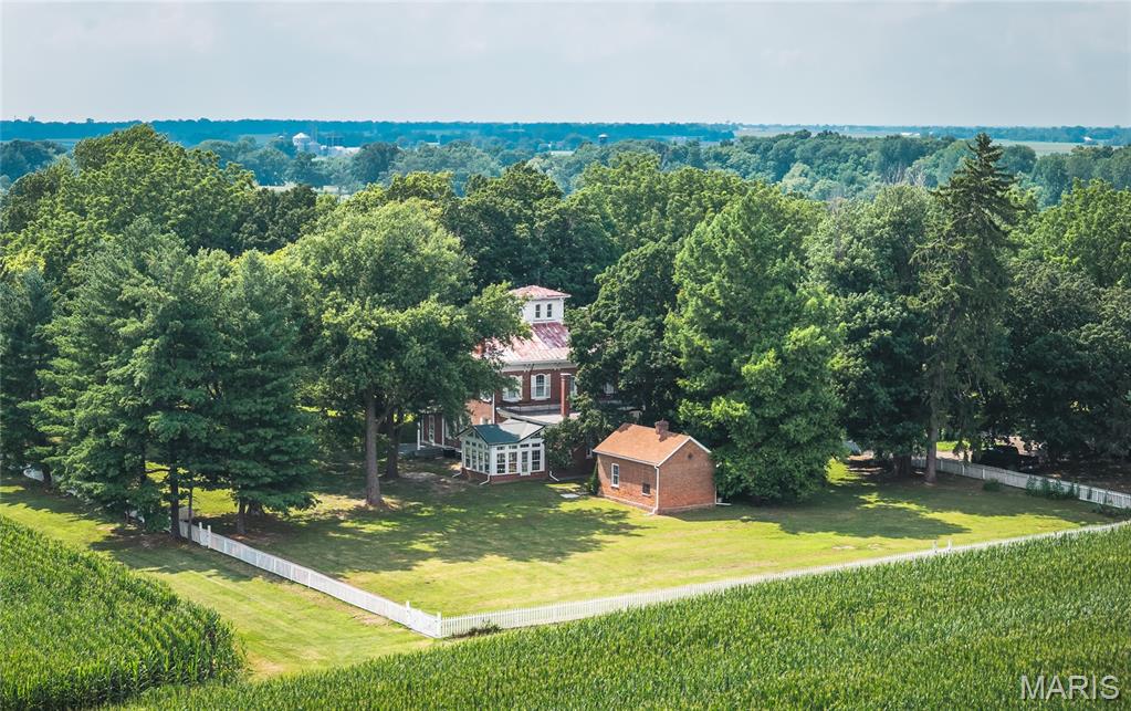 Steeped in history and timeless elegance, this extraordinary country estate, built in 1868, is a rare opportunity to own one of the area’s true architectural treasures. Meticulously maintained through the years, the home showcases the remarkable craftsmanship of a bygone era with the majority of its original features beautifully preserved. Expansive 12-foot ceilings, beautifully finished wood floors, multiple fireplaces, and a charming sunroom create a warm, inviting atmosphere filled with character at every turn.
A private, tree-lined driveway welcomes you to approximately 11 acres, where history and natural beauty come together. The grounds feature the original white picket fence, towering trees, a classic smokehouse, and an iconic red barn highlighted by impressive hand-hewn beams and an updated roof—offering endless possibilities for restoration, entertaining, or continued agricultural use.
Adding to the property’s versatility is a separate three-bedroom home, ideal for guests, extended family, rental income, or caretaker accommodations.
Located just minutes from the heart of downtown Edwardsville and only a 30-minute drive to St. Louis, this remarkable property offers the perfect balance of peaceful country living and convenient access to shopping, dining, and entertainment. Whether you’re searching for an exceptional private estate, a multi-generational property, or envision transforming this historic landmark into a boutique wedding or event venue, the opportunities are truly endless.