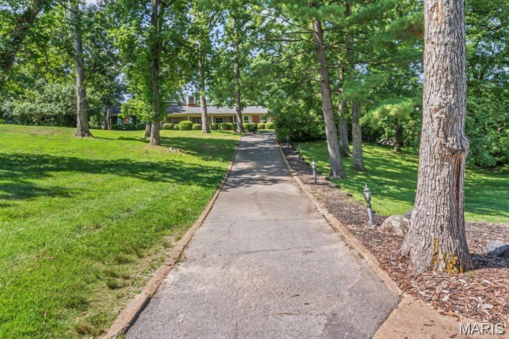 Set on a beautifully private 1-acre wooded lot, this distinctive ranch-style home offers true single-level living paired with an exceptional outdoor setting in a highly desirable location. Elevated within the neighborhood, the property enjoys a rare sense of privacy with no direct sightlines into the home or backyard.

Inside, the home features a spacious and functional layout with formal living and dining areas, a large family room with built-ins and dual fireplaces, and a split-bedroom floor plan designed for comfort and privacy. The vaulted primary suite includes a walk-in closet and a spa-style bath featuring a steam shower and its own dedicated hot water system.

The outdoor experience is a standout, anchored by a restored pool, expansive patio, and a shaded pavilion with suspended grill and fire feature — ideal for entertaining or relaxing. A separate spa house (approx. 272 sq ft) adds a unique wellness component with a jacuzzi, dry sauna, and steam room.

Also located on the property is a historic log cabin dating back to the 1800s, offering a rare and character-rich feature that is increasingly difficult to find. Whether preserved, restored, or reimagined, it adds a distinctive element to the property’s overall appeal.

Additional features include zero-step access throughout the home, solar panels to help offset energy costs, and a secluded courtyard. The expansive one-acre lot offers both space and seclusion while still being conveniently located near Covenant Seminary, CBC, The Priory, Visitation, Principia, Maryville University, and major medical campuses including Mercy and Missouri Baptist.

This property presents a strong opportunity for buyers seeking space, character, and long-term potential in a prime location. Home is being sold as-is and price reflects condition.