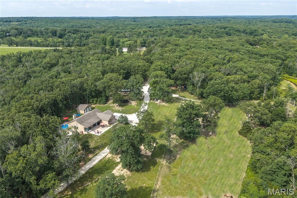 Discover the peace and privacy of your own secluded oasis with this custom-built, one-owner home nestled on 44+/- acres of serene countryside. Hidden from view with no visible neighbors, this tranquil sanctuary is surrounded by nature and accessed by a scenic private driveway, creating a true sense of escape from the everyday. Offering the perfect blend of comfort, recreation, and peaceful country living, this exceptional property invites you to relax, unwind, and enjoy the quiet beauty of your surroundings. The home features an open-concept design with vaulted ceilings, Anderson windows, commercial-grade flooring, and quality construction throughout, including glued and screwed subfloors. A 4-foot-wide hallway and staircase provide accessibility and spaciousness. The home offers 3 bedrooms and 3 bathrooms, plus a 4th room that does not qualify as a bedroom. The inviting main living area includes a wood-burning fireplace, while the finished basement features a wood-burning stove for added warmth and charm. The kitchen is designed for both function and style with granite countertops, custom cabinetry, stainless steel Maytag appliances, a large walk-in pantry, and abundant storage. Additional custom touches include barn doors, a bonus pool table room with a custom bar, and zoned HVAC for comfort and efficiency. The outdoor areas raise this property to another level. Enjoy peaceful mornings on the 6-foot-wide covered front porch or entertain family and friends across three separate patios. A 12x18 composite upper deck connects to a large composite pool deck surrounding the 54-inch-deep above-ground pool, creating the perfect setting to relax and spend time with family. The land is beautifully diversified with a large, stocked pond, natural spring, creek, ATV trails, and open areas for animals and recreation. Equestrian and livestock amenities include a 2-acre electric-fenced horse pasture, a brand-new loafing shed for horses, a 12x20 metal shed with a 60x80 run for goats or other animals, and a chicken coop with a fenced pen. For those needing workspace and storage, the impressive 40x40x15 metal building includes a concrete floor, 15x40 lean-to with a 50-amp RV hookup, 10x40 loft storage area, and dedicated workshop or office space. Additional features include a 15x26 tool shed with dog run and a 50x50x5 chain-link dog run. The property is equipped with a Generac whole-house generator connected to a 500-gallon propane tank, providing peace of mind year-round. The property is serviced by well water and septic. While currently one private estate, the land has already been subdivided by the new owner will have the potential to split further if desired. If you've been searching for a truly secluded property where you can enjoy nature, privacy, recreation, and modern comforts all in one place, this one delivers.