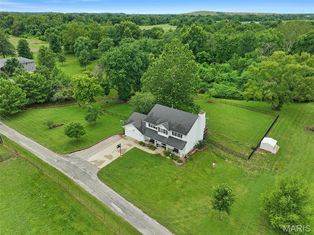 One of Edwardsville's best-kept secrets! Nestled along a quiet country road just minutes from downtown Edwardsville, shopping, dining, top-rated schools, SIUE & convenient hwy access, this beautifully maintained 2-story offers country charm & everyday convenience. From the covered front porch, enjoy picturesque views of rolling pasture & horses grazing nearby. Inside, an inviting foyer with open staircase welcomes you. Hardwood floors flow through the formal dining room, while the updated kitchen features white quartz counters, coordinating tile backsplash, dark stainless appliances, a pantry & sunny breakfast area with bay window & sliding door to access the huge composite deck. A shade sail creates the perfect spot to relax while overlooking the expansive fenced backyard, wooded backdrop & built-in firepit for evenings under the stars. Back inside, a living room with elegant fireplace, opens to a sitting room accented by beautiful wood molding, creating ideal gathering spaces. Upstairs, a spacious loft offers room to read, relax or unwind. French doors lead to the owner's suite featuring peaceful views, a walk-in closet, dual vanities with makeup area, linen closet, jetted tub & tiled walk-in shower. 3 additional bedrooms & a full bath complete the upper level. The finished lower level expands the living space with new LVP flooring, a large rec room with built-in entertainment shelving, dry bar, 1/2 bath & bonus room behind a sliding barn door. Classic design, meticulous care & an exceptional location!
