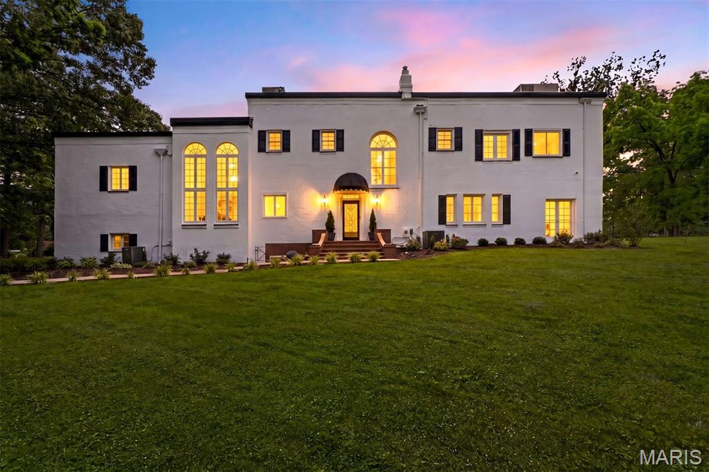 A striking Mediterranean Revival estate, where sun-washed stucco, soaring arched windows, and graceful symmetry create an atmosphere of effortless glamour. Infused with subtle Art Deco modernity, the residence evokes the golden age of luxury travel and Hollywood elegance—a home that feels equally at home on the hillsides of Southern California or tucked within a storied European enclave. Timeless, sophisticated, and undeniably captivating, it is a rare architectural treasure. Designed to capture both sunlight and serenity, French doors and expansive windows frame verdant views at every turn, blurring the line between indoors and out. Beyond the front door, a dramatic two-story foyer unfolds beneath a sweeping curved staircase, setting a tone of quiet grandeur and gracious hospitality. To one side, the living room glows with warmth and possibility. Anchored by a fireplace and opening to a charming cocktail porch and expansive brick terrace, it is a space made for evening gatherings, holiday celebrations, and conversations that linger long after sunset. Beyond, a tranquil den offers a peaceful retreat for reading, reflection, or simply watching the seasons change through expansive windows. The formal dining room, with its garden views and effortless connection to the outdoor entertaining spaces, invites memorable dinners beneath candlelight and celebrations both large and small. At the heart of the home, a beautifully reimagined kitchen blends timeless design with modern functionality. Custom cabinetry, premium appliances, and thoughtful finishes create a space where everyday moments—from morning coffee to Sunday brunch—feel elevated. Flowing seamlessly into the breakfast area, it serves as the welcoming heart of daily life. Upstairs, the primary suite occupies the entire western wing, offering a private sanctuary reminiscent of a boutique hotel retreat. A fireplace, sunlit sitting room, oversized dressing room, and spacious ensuite bath create a haven designed for rest and renewal. Additional bedrooms are generously proportioned, while a separate ensuite bedroom on the eastern wing provides exceptional privacy for guests, extended family, or an inspiring work-from-home retreat. While honoring its architectural heritage, the home has been thoughtfully enhanced for modern living. Recent improvements include a beautifully renovated kitchen and first-floor bath, refinished hardwood floors throughout, restored original doors and windows, two new HVAC systems, a tankless water heater, extensive interior and exterior painting, landscape enhancements, and numerous updates designed to improve comfort, efficiency, and peace of mind. Surrounded by beautifully refreshed grounds and a sense of uncommon privacy, this exceptional 4-bedroom, 3 full and 1 half-bath residence offers a rare balance of architectural significance and everyday livability. Here, grand entertaining and quiet mornings, historic character and modern luxury, all exist in perfect harmony. A timeless estate where European elegance, Hollywood romance, and the art of gracious living converge.
