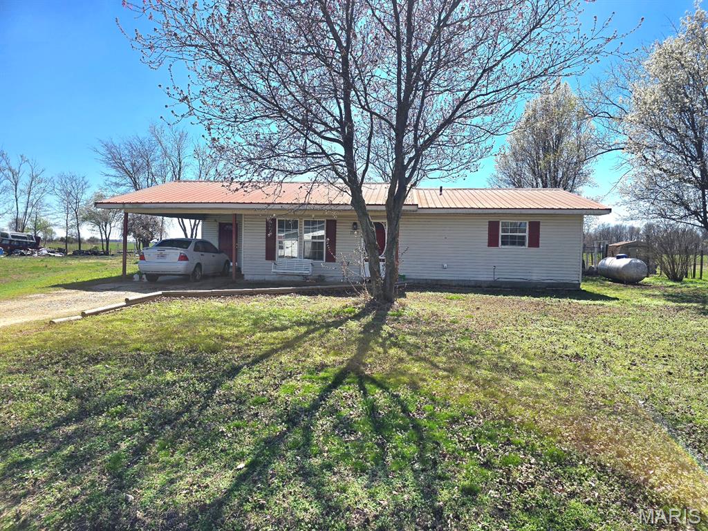 Are you searching for a home located out of city limits but you will have neighbors in your subdivision? Look no further.  his 3-bedroom, 1 -bathroom home is ready for you.  You'll find it sitting on a large lot on the outer "circle" on Sue Drive.  It has a covered, front porch -- perfect to relax and enjoy visiting with your neighbors, an attached carport, a detached garage/outbuilding -- perfect for storage or to be a workshop for your tools, and a large, fenced back yard which is a great area to enjoy a view of fields behind your new home.  Step in the front door and you will find you living room has a gas wall heater, and a "gate" separating the living area from the kitchen with a range top and a wall oven, dining area, and a separate laundry room.  Turn down the hallway and you'll find the bathroom and the three bedrooms.  Most of the rooms have had a fresh coat of paint and some minor repairs to help you move in without the trouble of painting. The LP tank stays with the home.