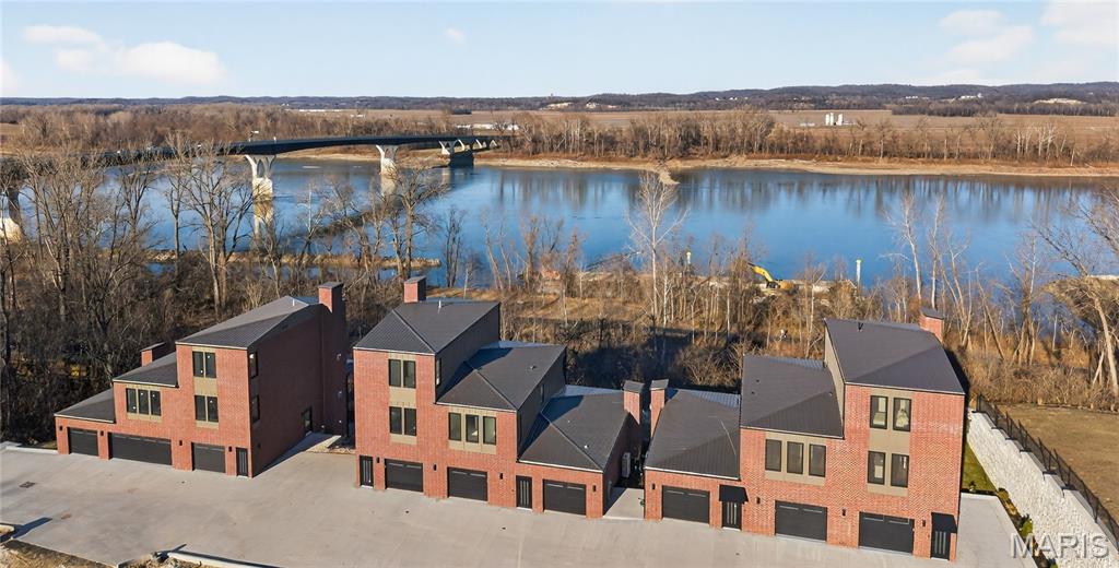 Welcome to The Bluffs at Bassora Place! This extraordinary, modern, 2,540 sq. ft., two-story townhome is perched on a scenic river bluff, where nature meets contemporary living in perfect harmony. From the moment you arrive, the architectural vision becomes unmistakable. Imported tilt-and-turn windows—a European hallmark of innovation & engineering excellence—frame the breathtaking Missouri River views. Every outward glance becomes a living masterpiece as nature’s timeless beauty unfolds before you. Step inside & discover an unwavering commitment to quality at every turn. The wide-open main level showcases true modern living with its seamless living/dining/kitchen design—an entertainer’s dream. Double doors open to an expansive deck, ideal for outdoor dining, hosting guests, or simply watching the boats go by. The kitchen is a standout feature, centered by a massive breakfast bar offering casual dining & abundant under-counter storage. Luminous quartz countertops define the space, while premium included Bosch appliances stand ready for culinary adventures. A well-designed butler’s pantry adds both storage & function—perfect for a coffee station—and cleverly tucks the refrigerator out of sight to maintain clean, uninterrupted kitchen lines. A stylish powder room & a stunning gas fireplace anchor the main living area, casting a warm glow on cool evenings. The lighted staircase guides you to the private upper level, where two luxurious bedroom suites await. The primary bedroom is a sanctuary unto itself. Here, sunrises & sunsets over the river create a beautiful start & end to the day. The ensuite bathroom exceeds all expectations with radiant heated floors—imagine stepping onto warm, sun-kissed tile even on the coldest mornings—along with an exquisitely tiled shower, relaxing soaker tub & double vanity. A thoughtfully designed custom closet system completes the space. An included Electrolux washer & dryer conveniently located in the hall, services both suites with ease. The fully finished walk-out lower level expands your living possibilities. With a full bath included, the space can function as a 3rd bedroom, a recreation room, or an office—your choice. Large windows ensure brightness, while the second gas fireplace adds cozy sophistication. Step out to the covered patio for additional outdoor enjoyment. Thoughtful upgrades are found throughout: zoned heating & cooling, engineered hardwood floors & a two-car garage equipped with an EV charging station & epoxy flooring are just a sampling of the exceptional features this home offers. The location adds yet another layer of appeal. Mercy Hospital is nearby, as is historic downtown Washington, dining & shopping. The Missouri River Bridge—your gateway to the region’s celebrated wine country & the Katy Trail—is just moments away. This is more than a residence. It is an invitation to live where exceptional craftsmanship meets nature’s majesty. Schedule your private showing today & discover what awaits you at The Bluffs at Bassora Place.