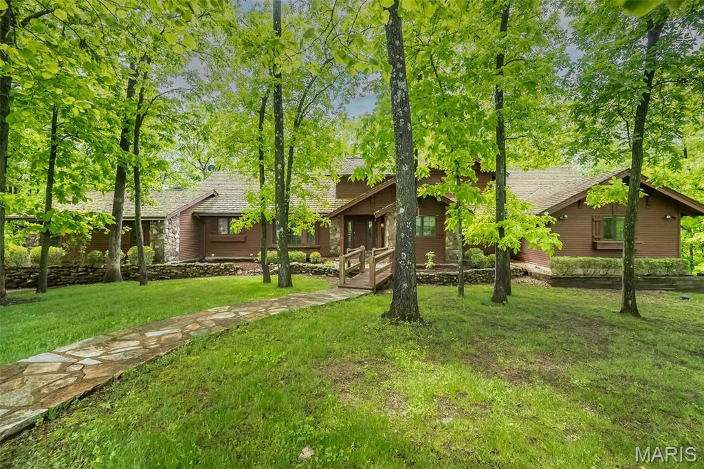 Tucked away on 5 breathtaking acres in the heart of Wildwood, this extraordinary lodge-inspired estate offers a lifestyle few properties can match. Surrounded by towering hardwoods and complete privacy, the setting feels more like a mountain retreat than a St. Louis address.

Inside, over 5,000 square feet of living space unfolds beneath soaring wood-beamed ceilings, dramatic timber accents, and walls of windows that bring the beauty of the outdoors inside. The stunning great room serves as the heart of the home, anchored by a floor-to-ceiling stone fireplace and framed by an impressive open staircase and loft overlook that create a true "wow" moment from the moment you enter.

Designed for both everyday living and unforgettable entertaining, the spacious kitchen offers abundant cabinetry, a center island, and seamless flow into gathering spaces filled with warmth and character. Multiple fireplaces, expansive living areas, and wooded views from nearly every room create an atmosphere that is both grand and inviting.

The main-level primary suite is a private sanctuary featuring a spa-inspired bath, generous walk-in closet, and peaceful views of the surrounding landscape. With 5 bedrooms, 4.5 baths, and a finished walk-out lower level complete with additional recreation space, there is room for family, guests, hobbies, and multigenerational living.

Step outside to discover expansive decks, winding pathways, mature trees, and a setting that changes beautifully with every season. Whether enjoying morning coffee among the treetops, hosting gatherings under the stars, or simply appreciating the quiet beauty of nature, this property delivers a rare sense of escape.

A truly one-of-a-kind offering where rustic elegance, timeless craftsmanship, and unmatched privacy come together on one spectacular Wildwood estate!

Please note that new custom home construction is ongoing in front of this property. This existing residence on Lot 7 is independently owned and is offered separately from the builder inventory. The surrounding luxury custom homes are anticipated to start around $2M+, further elevating the neighborhood's appeal.