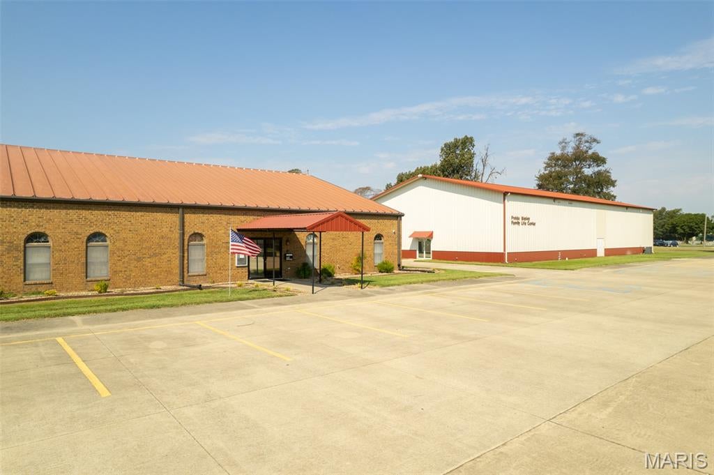 Rare opportunity to acquire a highly visible 5.1± acre commercial campus offering approximately 19,813 square feet of existing improvements, ample parking, and excellent potential for adaptive reuse, expansion, or future development.
The property includes two substantial buildings totaling nearly 20,000 square feet, along with approximately 2.4 acres of excess land. The site provides 69 striped concrete parking spaces, additional gravel parking, multiple access points, and excellent visibility from Stallcup Drive and Highway 62. Its location near the Highway 60/62 interchange, Walmart, Lowe’s, and surrounding commercial development makes it well positioned for a wide range of users.  Just 3 miles from the I-55 / I-57 interchange.
The 8,953-square-foot front building features a large auditorium, administrative offices, classrooms, meeting areas, restrooms, a small kitchen, and extensive storage. The adjoining 10,860-square-foot building includes a gymnasium or large multipurpose area, performance stage, commercial-style kitchen with ventilation hood, dining and gathering areas, classrooms, restrooms, and additional second-floor storage.
The property is currently configured as a religious and community facility; however, its size, layout, parking, excess land, and reported IL Light Industrial zoning create possibilities for educational, institutional, recreational, office, event, service, or other commercial uses. All proposed uses, zoning, building measurements, acreage, and development plans are subject to independent verification and applicable governmental approval.