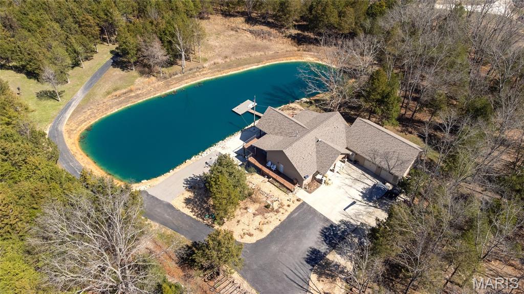 Enjoy vacation living EVERYDAY! Just outside of St James, Missouri, this incredible A-Frame type home sits on 5 acres right on the edge of a manicured and fully stocked lake. In fact, outside living is a major focus, to include a wrap-across deck and lower patio, professional landscaping to include a large waterfall pond. There are above ground garden plots, an established grapevine and a feeding area for the deer. Inside you'll find everything you need to escape the world and enjoy life in the country.  Main level primary suite, custom kitchen w/ solid wood cabinets, solid surface counters, walk-in pantry, coffee bar and WINDOWS galore. There's even more storage in the large laundry room w/ cabinetry similar to a butlers pantry. Also on the main level is a half bath and a nice office/possible 4th bedroom. Downstairs is where you can send your extra friends to visit in the family room w/ fireplace or cook up a bigger dinner w/ the 2nd full kitchen set-up. There are 2 more bedrooms and baths and another non-conforming sleeping area that could easily be made into a small theatre or work out room. There's even a 2nd laundry set up downstairs. Additional features include a hot tub, lit flag pole, dock for fishing and SO much more. Be sure to schedule your private showing today!