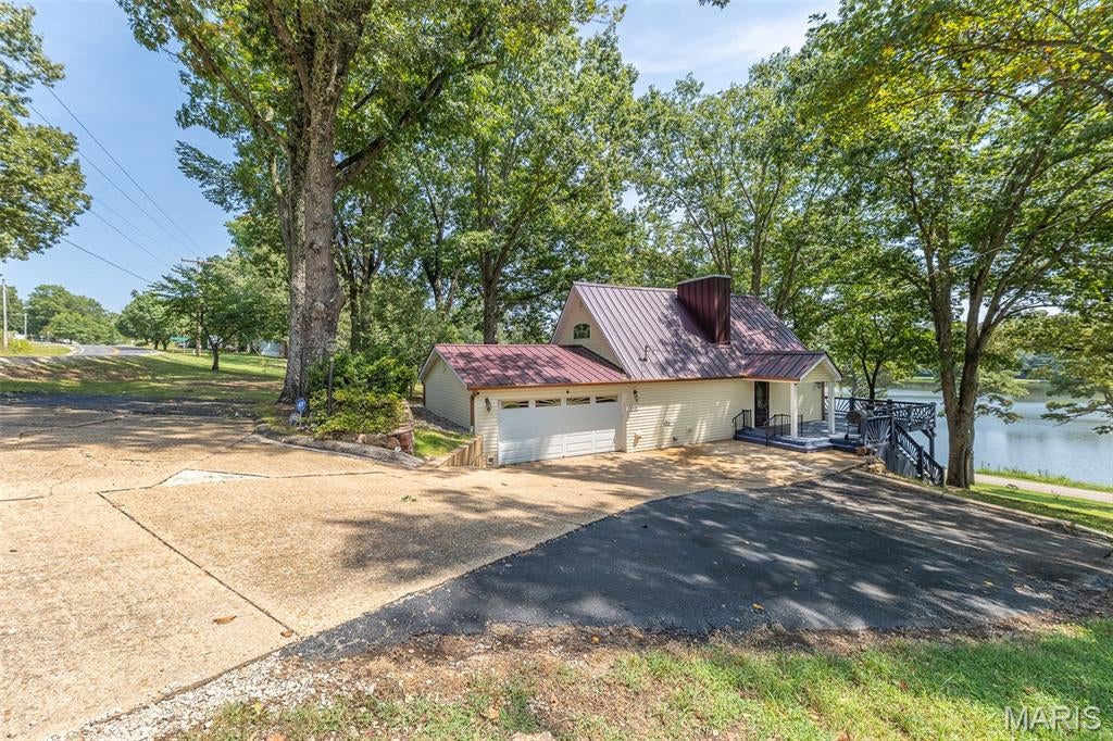 Wouldn't you love to feel like you're on vacation while relaxing at home? Just minutes from town along scenic W Highway, this beautifully maintained home offers just that, with the rare combination of privacy, convenience, and stunning lake views! Tucked away off the road, this home feels like a hidden retreat you might never know was there unless you were looking for it. With several recent updates, such as a new metal roof, HVAC system, guttering, freshly painted deck, updated kitchen appliances and solar-tinted windows, this property is ready to move in and enjoy without the stress! 
Outside, the expansive wrap-around deck creates the perfect setting for entertaining, sipping your morning coffee, or unwinding while taking in the peaceful lake views and gently sloping, shaded yard. The attached garage offers plenty of room for storage, while additional parking ensures room for guests. 
Inside, you’ll find an incredibly inviting atmosphere with beautiful hardwood floors, oak cabinetry, exposed ceiling beams with accent lighting, and a cozy gas fireplace on the main level. The kitchen is designed for everyday living and entertaining, featuring new KitchenAid appliances, durable hard-surface countertops, and abundant prep space. French doors provide easy access from the kitchen to the deck, bringing the beautiful surroundings into the heart of the home.
Each level offers its own private retreat, with an en-suite bedroom on every floor. The main-level bedroom features French door access to the side deck, soaking tub, and a walk-in closet. Upstairs, you'll find another comfortable suite complete with a newly tiled shower. The lower level provides even more flexibility, with a bedroom connected to an additional living or entertaining area and a walk-out basement offering easy access to the outdoors and additional, separate storage area.
With its peaceful setting, serene lake views, generous outdoor living spaces, and thoughtful updates throughout, this home offers the feel of a vacation getaway while remaining just minutes from everything Poplar Bluff has to offer. This is truly special property that invites you to slow down, relax, and enjoy the view! The home is being sold partially-furnished with a list available upon request.