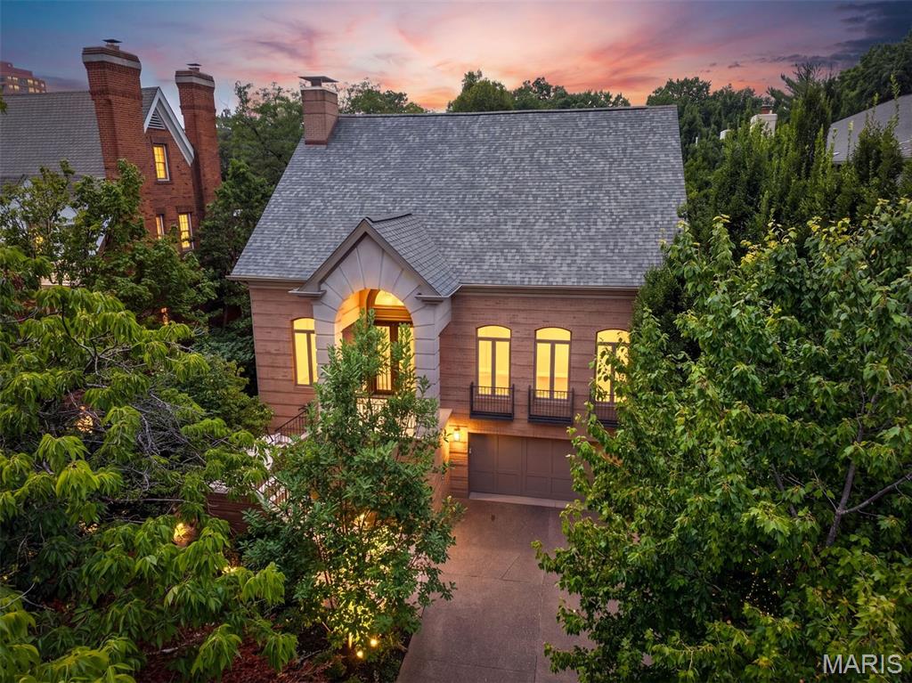 In the heart of Old Town Clayton, this distinguished residence offers a rare blend of architectural drama, effortless luxury and extraordinary privacy. From the moment you enter, the home makes its intentions known. A dramatic foyer unfolds beneath a graceful elliptical barrel-vaulted ceiling, while pale brushed-oak floors laid in a striking herringbone pattern draw the eye toward the beautifully appointed rooms beyond. Designed for both grand entertaining and intimate daily living, the main level flows effortlessly from an elegant dining room - made for candlelight, cocktails and long dinners with friends - into a light-filled living room with soaring ceilings, a gas fireplace and an open staircase. The generously sized kitchen and breakfast room invite lingering mornings and lively evenings, with an oversized peninsula, abundant storage and beautifully refreshed cabinetry. Nearby, the enchanting all-season sunroom opens the home to lush, professionally landscaped grounds, creating a private retreat in every season. Tucked away in its own serene wing, the main-level primary suite opens directly to the gardens and features two organized walk-in closets and a spacious bath with jetted tub and separate shower. A handsome den with a second gas fireplace offers an intimate setting for quiet evenings or late-night conversation. Main-level laundry, powder room and an elevator provide ease without sacrificing style. Upstairs, two additional bedrooms and a Jack-and-Jill bath create gracious accommodations for family. The expansive finished lower level extends the living space with a family room, recreation room, exercise or flex space, full bath, bar and private fourth bedroom - ideal for guests, an au pair or multigenerational living. Recent improvements include a new roof, new hardwood and carpeting throughout, two new HVAC systems, fresh interior paint, professionally painted kitchen, laundry and primary bath cabinetry, and new cabinetry in the lower-level bath, bar and bedroom. Set amid lush, established landscaping with a rare three-car tandem garage and Taylor park just beyond - moments from Clayton’s finest dining, shopping and cafes - this stately residence is gracious, sophisticated, and quietly seductive.