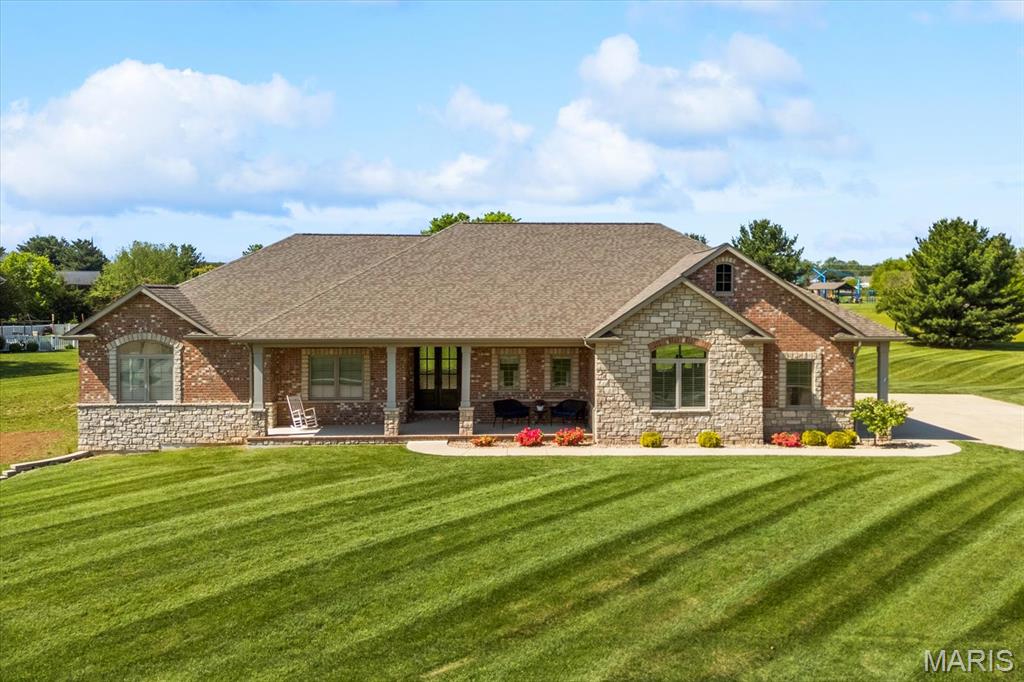 A masterpiece of craftsmanship and refined living, this 3 sides-brick-and-stone estate commands attention from the moment you arrive. Set foot on an impressive 1.63-acre double lot. The home blends architectural integrity with modern luxury, offering a lifestyle defined by comfort, sophistication, and enduring quality. A stately double-door entry welcomes you inside, where hand-scraped hardwood floors flow gracefully throughout the main level, setting a warm yet elevated tone. Constructed with 2x6 framing, casement windows, and 9-foot walls throughout, the home feels both substantial and airy. The living room has 11' ceilings and a striking gas stone fireplace create a dramatic focal point, while oversized 8' x 8' patio doors in both the dining room and garage invite natural light and seamless indoor-outdoor flow. The kitchen is a true culinary showcase, anchored by a Sub-Zero refrigerator, 48" Wolf hood, and Wolf gas stove—a dream for the passionate cook. An abundance of sleek cabinetry,  Cambria Quartz countertops, and a stainless-steel apron sink elevate the space, while under-cabinet and overhead lighting add a soft, luxurious glow. A wrap-around cabinet layout maximizes storage and workspace, and the walk-in pantry with deluxe shelving ensures every culinary tool has its place. Cambria Quartz countertops are located in laundry room and mud room. The covered back patio extends the living space outdoors, perfect for quiet mornings or elegant entertaining. The primary suite is a private retreat, offering a serene sitting area/office with a private patio, a 9' ceiling with 1' tray, and a large shower designed for spa-level relaxation. The suite’s thoughtful layout and refined finishes create a sanctuary of comfort and style. At the front of the home, a second bedroom suite provides exceptional privacy for guests, complete with its own full bath and tile zero-entry shower. With 3 bedrooms and 3.5 baths, the home balances luxury with practicality. Mechanical and structural features further distinguish this residence: a central vac rough-in, an AprilAire humidifier, basement access through the garage, and a gas hookup for a garage furnace. The professionally finished 4-car garage impresses with two 18' doors, a sink, zero-egress access, and ample space for vehicles, hobbies, or storage. The basement has 9' celings with large look-out windows and a bathroom rough-in. Outside, the brick mailbox and expansive grounds enhance the home’s commanding presence, offering endless possibilities for outdoor living or future enhancements. This estate is more than a home—it is a statement of luxury, craftsmanship, and thoughtful design, created for those who appreciate elegance without compromise. The second lot offers additional privacy and a water meter for future plans. Make your appointment TODAY!