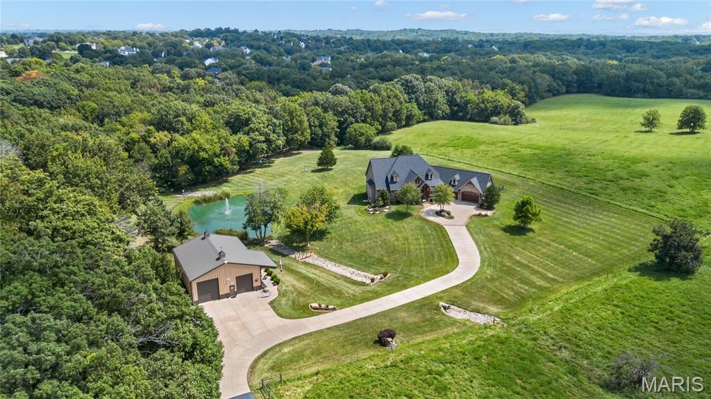 Soaring ceilings, wide plank hardwoods & timber beams define the rustic elegance of this L R Spraul-design Estate. Tucked away on 10.2 scenic acres that include a riding trail, stocked pond with fountain and 45’ x 40’ outbuilding, perfect for RV or additional vehicle storage. Vaulted porch entrance with architectural pillars & extraordinary 8’ glass-paneled door leads to dramatic foyer with stone accent wall and arched entryways that open to private study and beautifully appointed dining room with tray ceiling & built-in wall unit. A beamed cathedral ceiling with timber trusses, lighted display cases and floor-to-ceiling stone fireplace set the tone for the stunning great room. The designer kitchen with granite countertops, custom white cabinetry, stone cooking alcove, premium stainless steel appliances and 9’ center island flows into the light-filled breakfast room. A barrel-vaulted entryway leads to the coffered primary bedroom suite with stacked stone fireplace, customized walk-in closet & spa-like bath with soaking tub. A second ensuite bedroom completes the main floor living quarters. Lower Level entertainment space includes recreation room with stone fireplace and 2nd kitchen with suede granite wet bar plus workout room, 3rd bedroom and full bath. Atrium doors open to outdoor living area with firepit and covered and open patios surrounded by landscaped gardens. Conveniently located near shopping, restaurants, Weldon Spring Park and Katy Trail with easy access to major highways & Chesterfield Valley.
