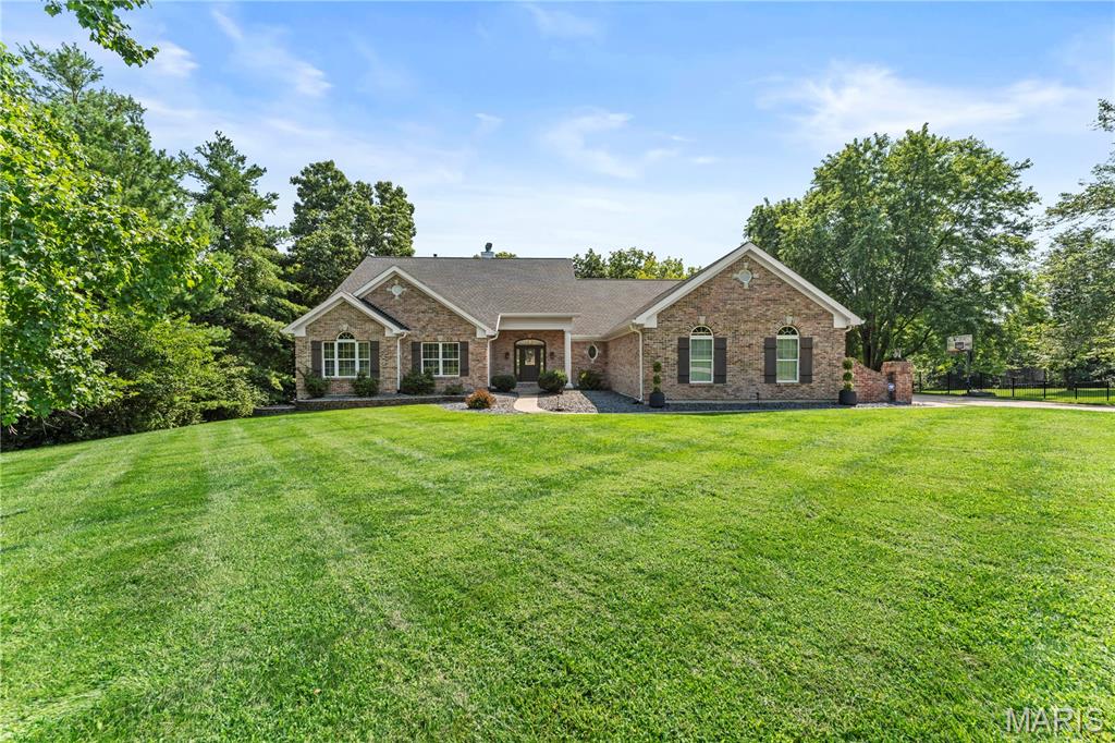 Set on three private acres in Forest Lake Estates within the Francis Howell School District, this 5300+ square foot atrium ranch has been reimagined in its entirety. The kitchen, dining room, great room, bathrooms, flooring, lighting, and paint have all been renewed, allowing the home to feel newly built while retaining the scale and setting only a mature lot can offer. Inside, the great room rises beneath a vaulted ceiling, where a wall of windows draws the surrounding acreage into everyday view. The kitchen continues that sense of openness with its own vaulted ceiling, 42 inch cabinetry, quartz countertops, a center island, coffee bar, and walk in pantry. A half bath and laundry room are conveniently located nearby. Warmed by a gas fireplace beneath a vaulted ceiling, the breakfast room opens through an atrium door to a composite deck. Stairs lead to the saltwater inground pool below, quietly set within the landscape. The open dining room, also crowned by a vaulted ceiling, lends a natural sense of occasion to gatherings both intimate and grand. The primary suite is a retreat in itself, featuring a vaulted ceiling and fully renovated en suite bath. A full bath serves the remaining bedrooms, while an additional half bath is positioned near the great room. The walkout lower level extends the home into a world of its own, offering a family room, recreation room with golf simulator, additional bedrooms, a full bath, bar, and an expansive fitness space anchored by an infrared sauna. It is a level suited equally to quiet restoration and entertaining at scale. The setting completes the picture. A four car, side entry garage accommodates a serious collection, while three acres, with the pool at their center, create a rare sense of seclusion within the Francis Howell corridor, an oasis glimpsed from beyond the tree line but fully experienced only from within.