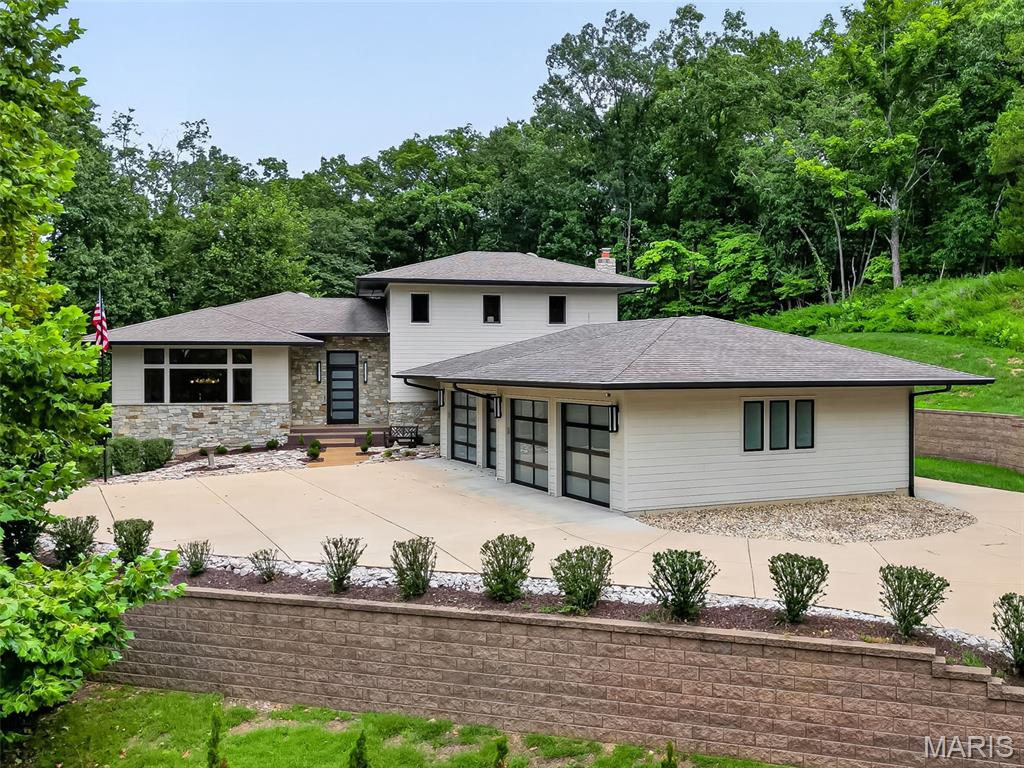 Secluded high on a private hilltop surrounded by 3.3+ wooded acres, this extraordinary 4,117 sq. ft. home built by Hibbs Custom Homes offers incredible privacy, beautiful views and truly one-of-a-kind design. Recognized as a 2019 Custom Home of the Year by the Home Builders Association, this striking 1.5-story home blends mid-century modern style with exceptional craftsmanship and thoughtful custom details throughout.

Walls of windows bring the outdoors in and showcase the beautiful wooded setting while filling the home with natural light. At the heart of the home is a showpiece kitchen designed for both everyday living and entertaining. A waterfall-edge island anchors the space, surrounded by custom full-height cabinetry with extensive storage, crown detailing and illuminated glass-front displays. A distinctive mosaic tile backsplash adds color and texture, while a Wolf gas range with pot filler and stainless hood, Sub-Zero refrigerator and built-in appliance wall complete the space. Multiple prep areas add functionality, while statement lighting and warm wide-plank wood flooring complement the home’s clean-lined, mid-century modern design.

The kitchen opens beautifully to the adjoining dining and gathering spaces, creating an open, light-filled layout with incredible views from nearly every angle. The inviting hearth room offers a more intimate place to gather with a custom bar and second gas fireplace.

The main-level primary suite is a true private retreat surrounded by beautiful views. The spa-inspired bath features a freestanding soaking tub, impressive oversized walk-in shower with built-in bench and multiple shower fixtures, extensive tilework, radiant heated flooring, and custom vanity cabinetry.

One of the home’s most impressive features is the incredible loggia with retractable glass doors, screens and vinyl walls, plus ceiling-mounted heaters for extended-season enjoyment. Overlooking the heated saltwater pool and private wooded surroundings, it creates a seamless connection between indoor and outdoor living. 

Additional features include integrated Lutron lighting controls with programmable keypads throughout, geothermal system, a custom main-floor laundry, a water filtration system, a dedicated drop zone with built-in nook and lockers, and an oversized 4-car garage.

Truly one of a kind, this St. Albans Forest home offers the privacy of a secluded wooded retreat combined with distinctive architecture, exceptional custom finishes and incredible spaces designed for both everyday living and entertaining.