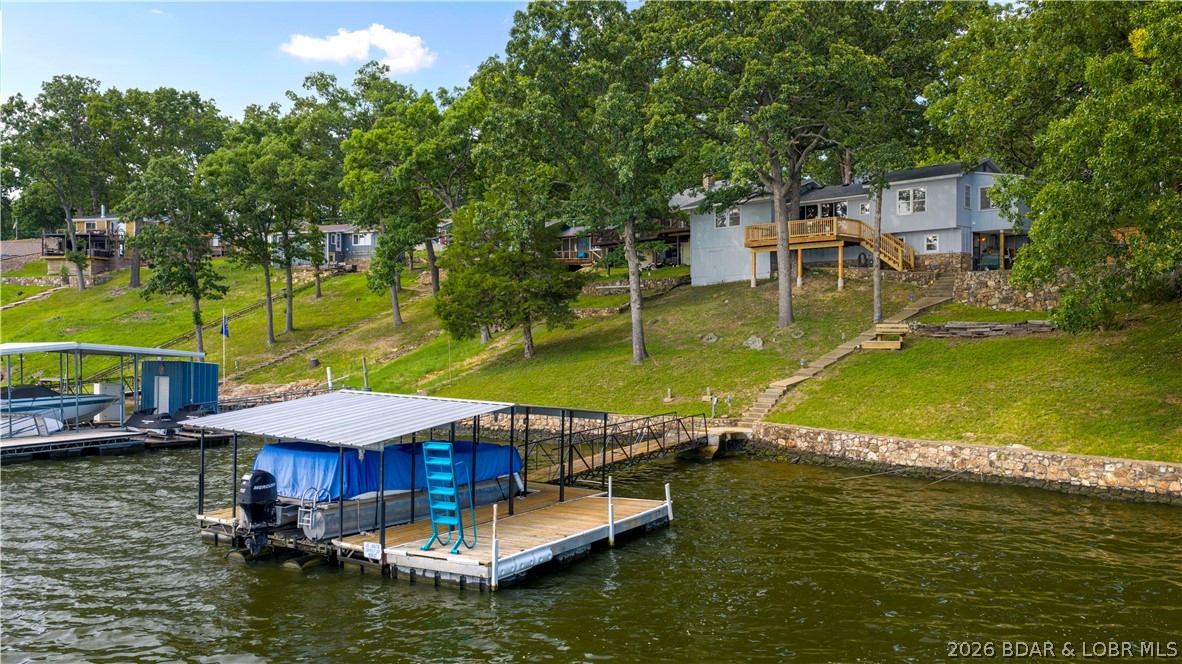 There's something familiar about this lake house. Maybe it's the knotty pine walls, the wood-burning fireplace, or the way the living and dining rooms look out toward the water. The main level offers a lakeside primary suite with its own bath, along with two additional bedrooms and a second full bath. Just off the dining area, sliding doors open to a spacious 13x20 deck built around one of the property's mature oak trees. It's an easy place to settle in and take in the wide channel view. One of the additional lakeside bedrooms also opens directly onto the deck. The kitchen includes a breakfast nook, while built-ins, generous closets, storage beneath the home, and a detached 16x26 garage with workshop space provide room for everything that comes with lake life. A gentle walk leads to the dock with a 12x24 boat slip with lift completing a property that still feels like the Lake of the Ozarks many people remember. Tritoon available to purchase. Home comes completely furnished.