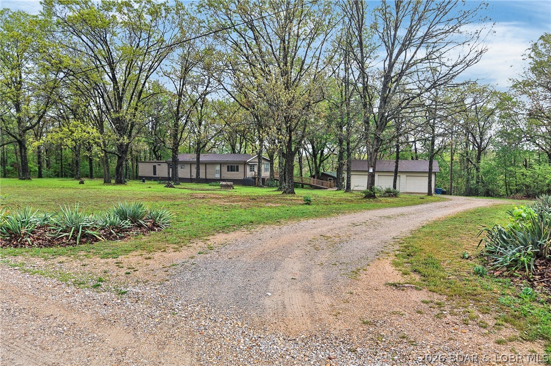 This home consists of a mobile with an addition home built around it on a concrete foundation, nestled away from the road in a BEAUTIFUL PARK-LIKE SETTING ON 6.01!! Including the addition, it now offers over 1,600 sq ft of living space! The layout consists of a 3-bedroom, 2-bath, a spacious living room, and a beautiful updated kitchen that includes stainless steel appliances, plenty of cabinetry,  and a combo dining room, plus a 4-season sunroom with a built-in bench, A DETACHED 3-CAR GARAGE, and a LOVELY OFFICE/ CABIN great for your guests! with utilities including septic ( needs a finishing touches), a man cave /She-shed with propane heat, water, and electric. Among the updates are a new roof with a transferable warranty, a deck with a ramp, updated LED lighting, sinks and faucets, kitchen countertops, and 2 additional laundry connections (the 3rd bedroom is currently being used as a laundry area). Dusk-to-dawn security lights, newer siding at the front of the home, newer LVP flooring throughout the home, and numerous hydrants throughout the property. Enjoy the beautiful setting. This property is located near the Bennett Spring Conservation Area, home to abundant wildlife.