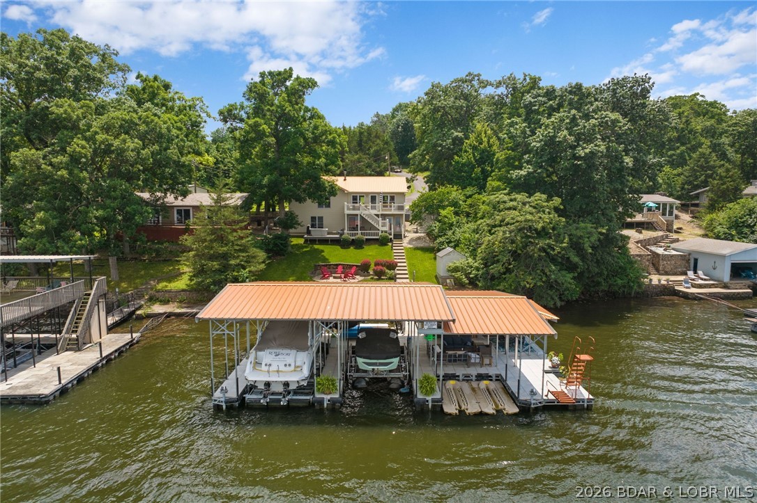 The ultimate Lake of the Ozarks retreat awaits at this premier lakefront property in Gravois Mills. From the moment you arrive, the gentle topography and minimal steps to the water set the stage for effortless lakeside living. Inside, the beautifully updated home features four bedrooms, two full bathrooms, and one half bathroom, complemented by a spacious attached two-car garage. High vaulted ceilings and a brilliant wall of windows anchor the main living area, framing incredible views and filling the space with natural light. The stunning kitchen stands out with custom cabinetry, premium stainless steel appliances, and a breakfast bar. Step outside to find your private paradise, complete with a lakeside stone fire pit and a state-of-the-art dock. This incredible dock features three slips, including two for boats and one for personal watercraft, alongside a massive covered patio with remote-controlled roll-down shades and a built-in outdoor bar. Currently on a successful vacation rental program with an established rental history, this turnkey property offers the perfect opportunity to roll over a thriving investment or enjoy your own private sanctuary.
