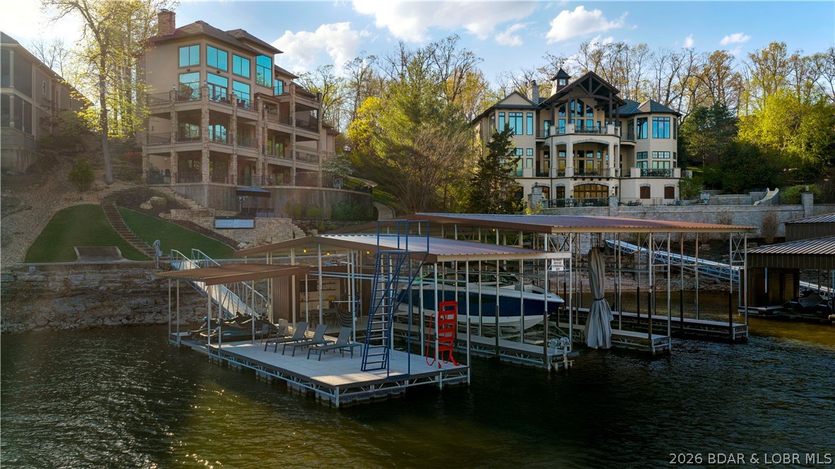 Experience luxury waterfront living at Lake of the Ozarks in this 7,600+ sq ft estate located in the prestigious, private gated Villages subdivision. Situated on one acre with 152 ft of shoreline, this home offers stunning lake views from every bedroom. Designed for entertaining, it features four levels accessible by elevator, a top-floor master suite, two kitchens, multiple bars, two ice makers, and a whole-home sound system. Outdoor living includes four levels of patios, a pool, hot tub, and fire pit overlooking the water. The massive dock includes two 16x44 slips, one 12x32 slip, and a bar area.  A golf cart path provides easy access to the dock. This turnkey home comes fully furnished with high-end designer furniture included in the price. Additional features include a four-car garage with car lift and golf cart. This is more than a home—it’s a private, gated waterfront retreat where every detail is designed to elevate your lifestyle.  For a full list of features, upgrades and updates, please reach out to your REALTOR.  Seller is also willing to sell their 2021 Cobalt boat with lift and cover, plus two 2023 Yamaha VX Cruiser PWC with lifts.