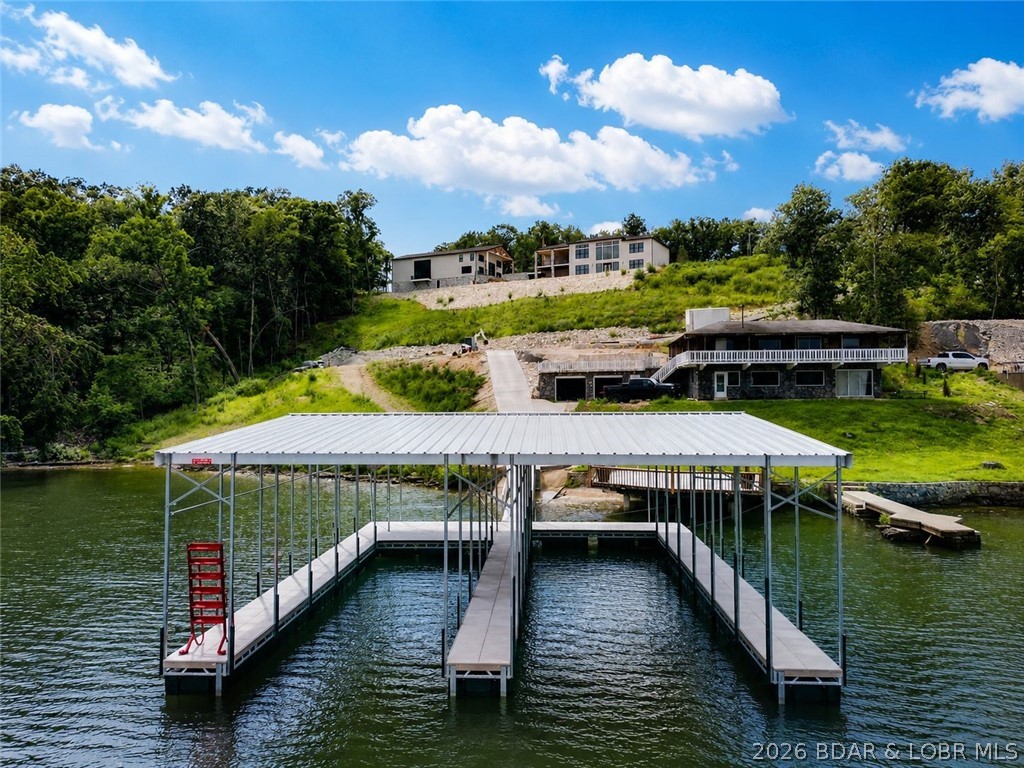Exceptional Lake of the Ozarks retreat offering luxury, functionality, & outstanding waterfront amenities. Now being sold w/ an additional lakefront lot featuring 156 feet of shoreline, expansive main channel views, cove protection, & brand-new two-slip dock with 16x50 and 14x42 slips. Designed to maximize the views, the home showcases quality craftsmanship, an open-concept layout, & abundant natural light. The spacious kitchen features a butler’s pantry and large windows overlooking the lake. The primary suite offers a luxurious bath and custom closet, while additional bedrooms also include custom closet systems. Outdoor living is highlighted by a private pool overlooking the water, creating an ideal setting for relaxation and entertaining. A standout feature is the detached shop with three garage bays, loft, grilling station, and private bath. The walkout lower level includes a second living area and full kitchen, providing excellent space for guests and gatherings. Conveniently located just minutes from the HH Strip w/ no HOA restrictions, this property offers privacy, exceptional views, extensive waterfront, & an unmatched lake lifestyle.